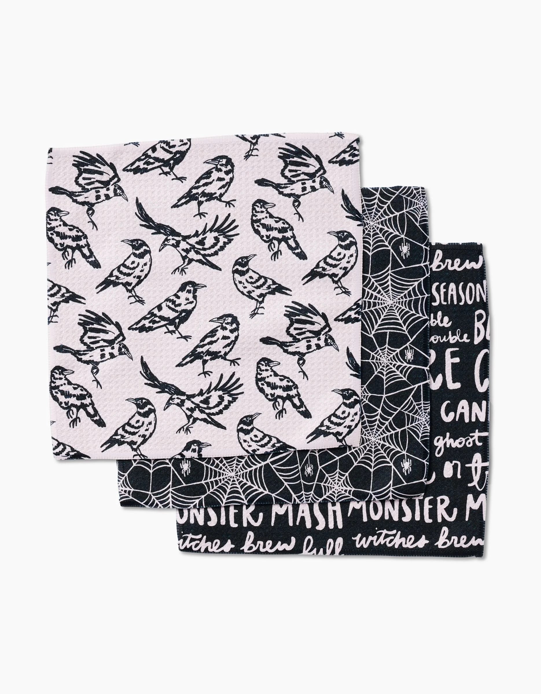 Kayla Ann’s Booos set includes three folded dish towels: the front has a black and white bird pattern, the middle features spiderwebs, and the back displays Halloween words on black—all in durable Geoweave fabric.