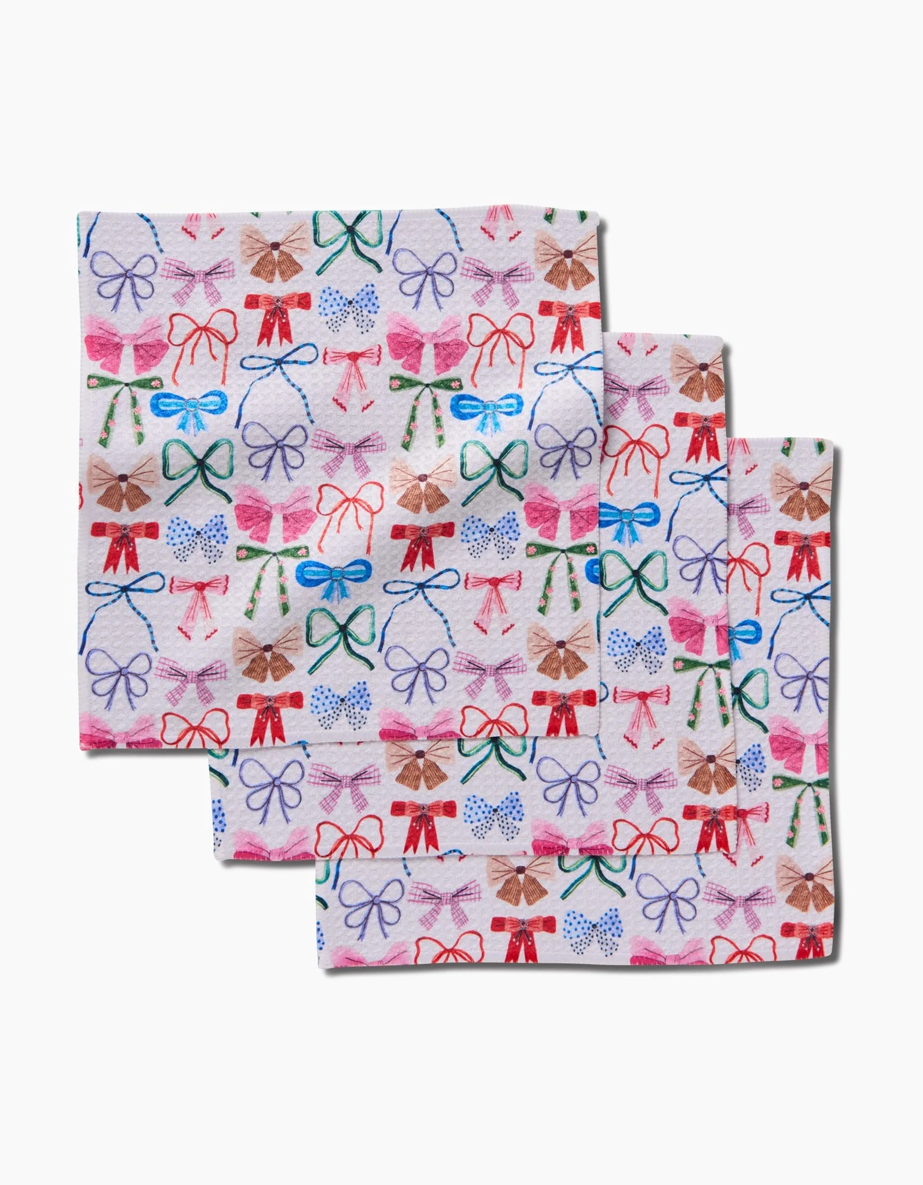 Three folded Daria Solak Bows dishcloths stacked with a colorful bow pattern in red, blue, brown, and pink on white. Crafted using innovative Geoweave Technology.