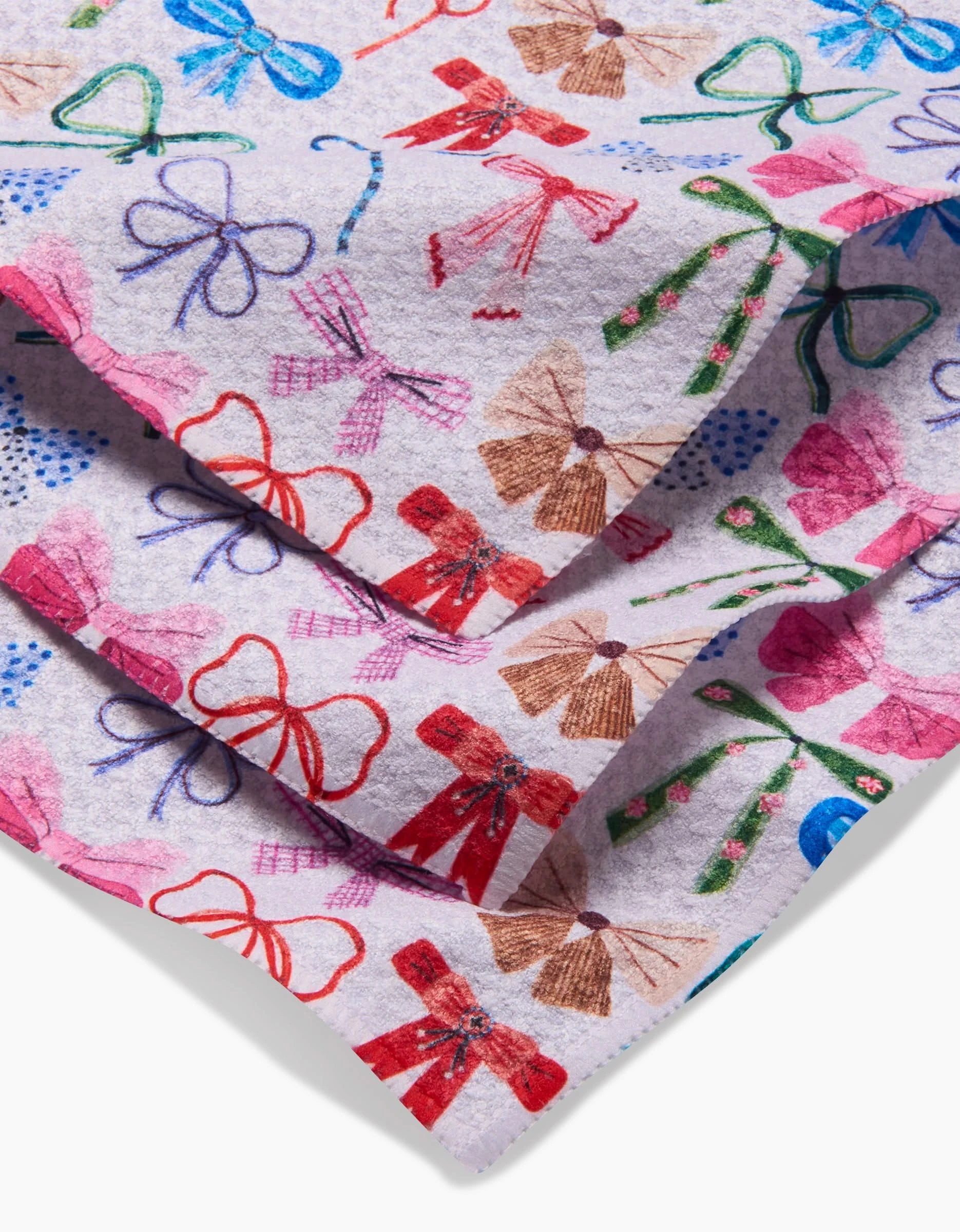 A close-up of folded white fabric from Daria Solak’s Bows, made with recycled materials and featuring a lively pattern of colorful, hand-drawn bows in red, pink, blue, green, and brown.