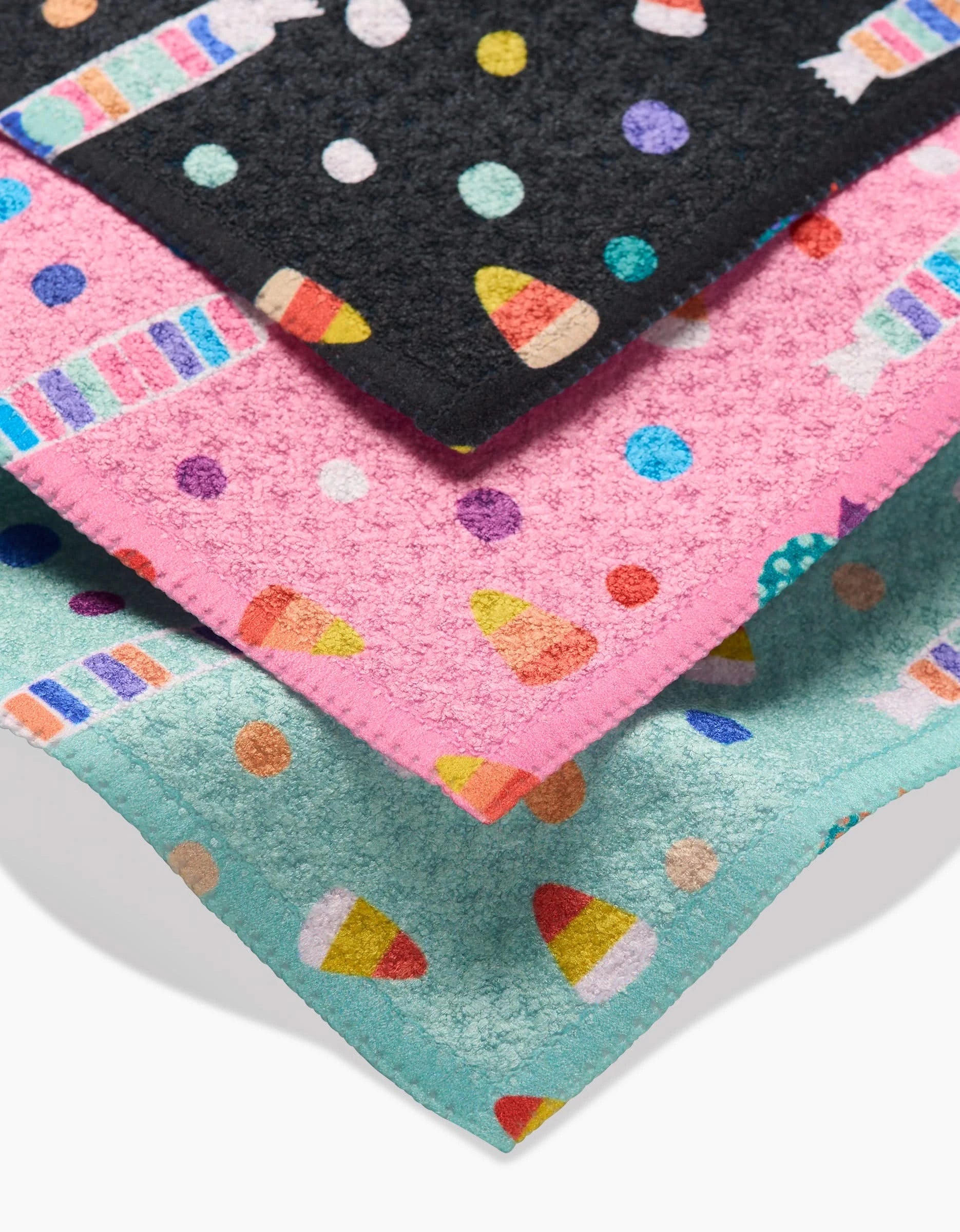 The Rebecca Bobko Candy Rush set includes three eco-friendly Geoweave dishcloths in black, pink, and teal, each featuring vibrant patterns of candy corn, polka dots, and striped candies.