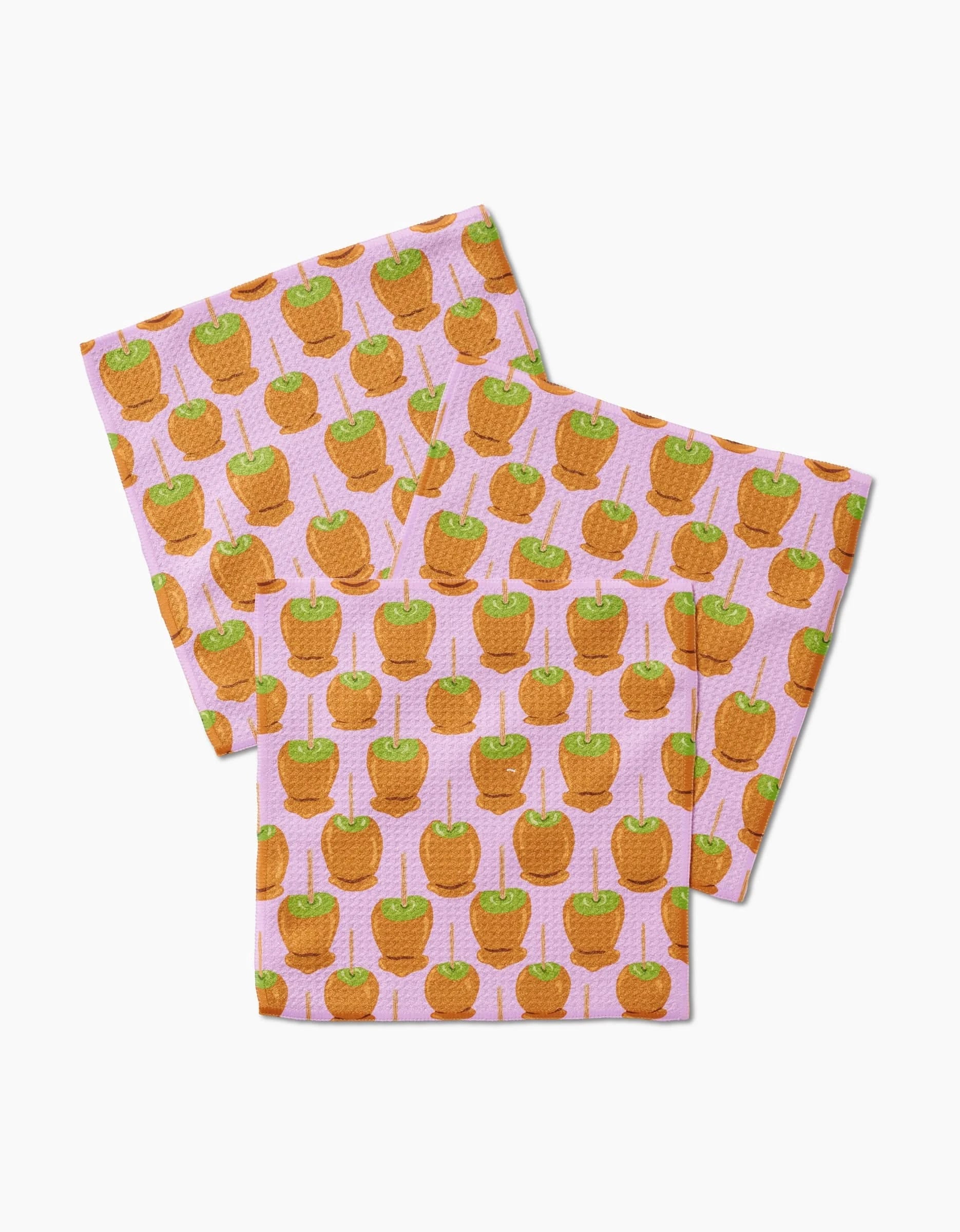 Three folded Elisabeth Wing Caramel Apple cloth napkins made with Geoweave fabric, featuring a repeating caramel apple design on sticks over a pink, subtly dotted background.