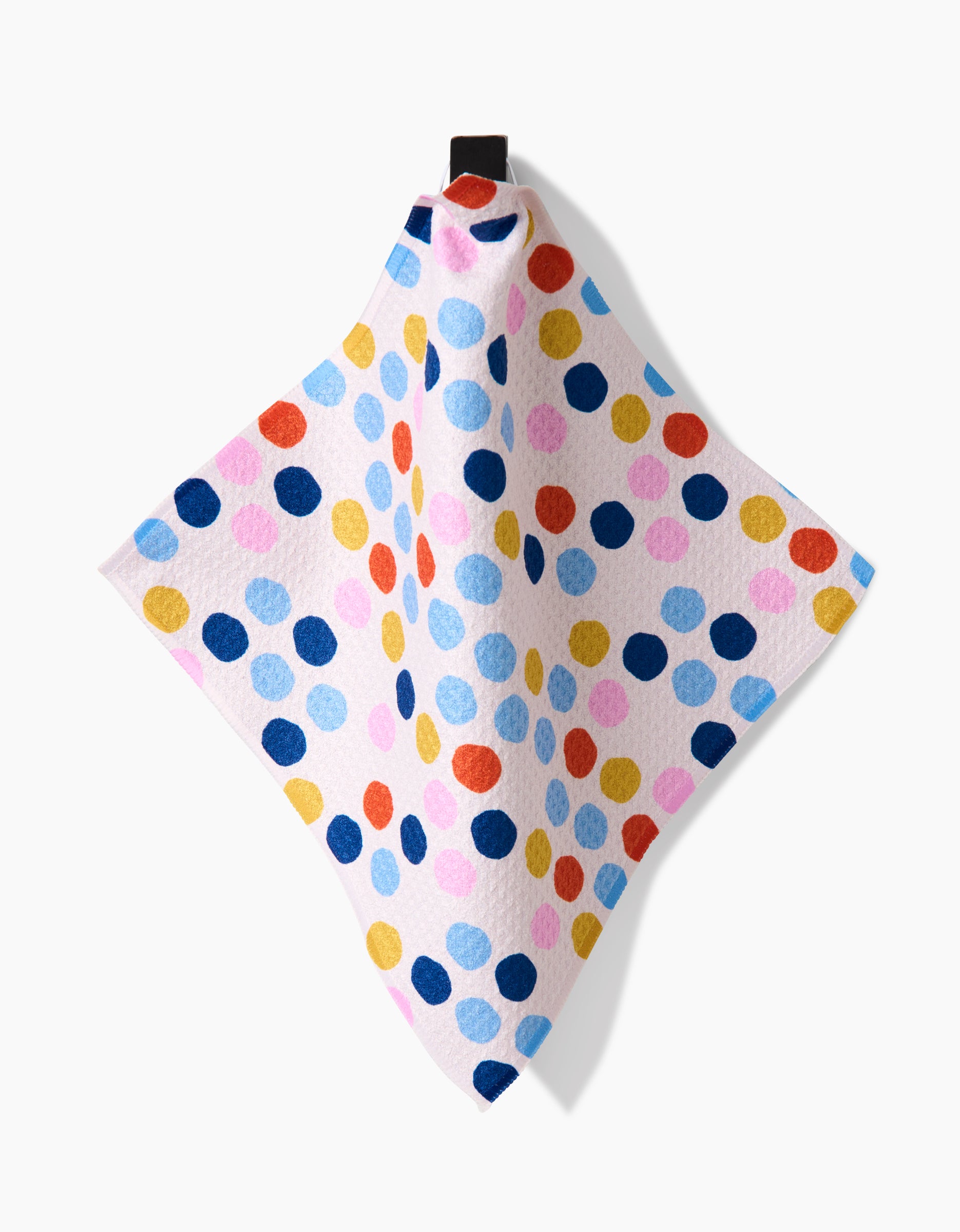 The Lizzie Clark Carnival Fling Geoweave dishcloth, made from recycled materials, showcases large polka dots in blue, yellow, red, and pink on a light background and hangs from a black loop against a white backdrop.
