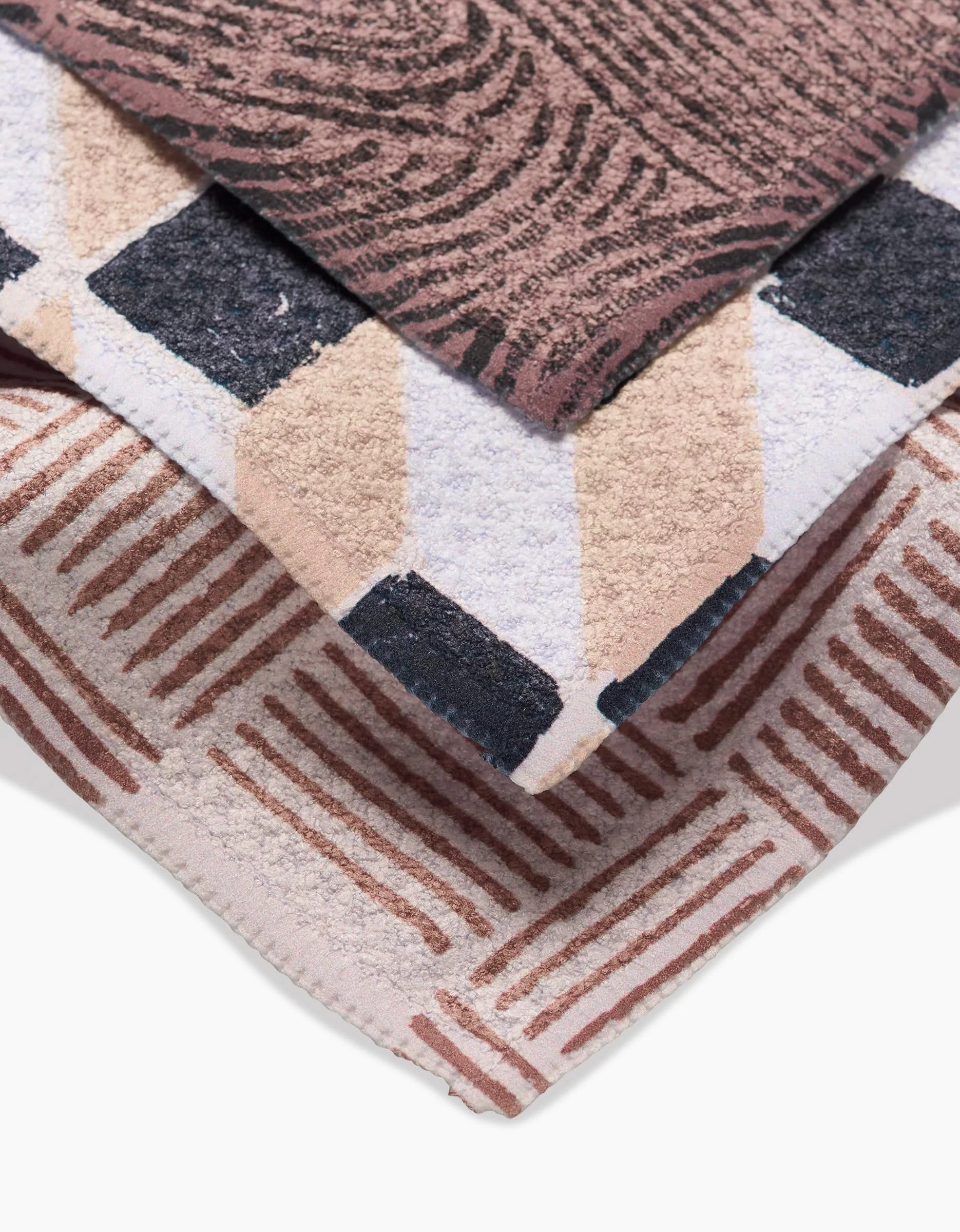 Three overlapping Chiseled dishcloths by Studio Jeannot, crafted with Geoweave fabric: top shows a pink and brown swirl, middle has beige and black diamonds, bottom features a brown grid—designed for style and durability.