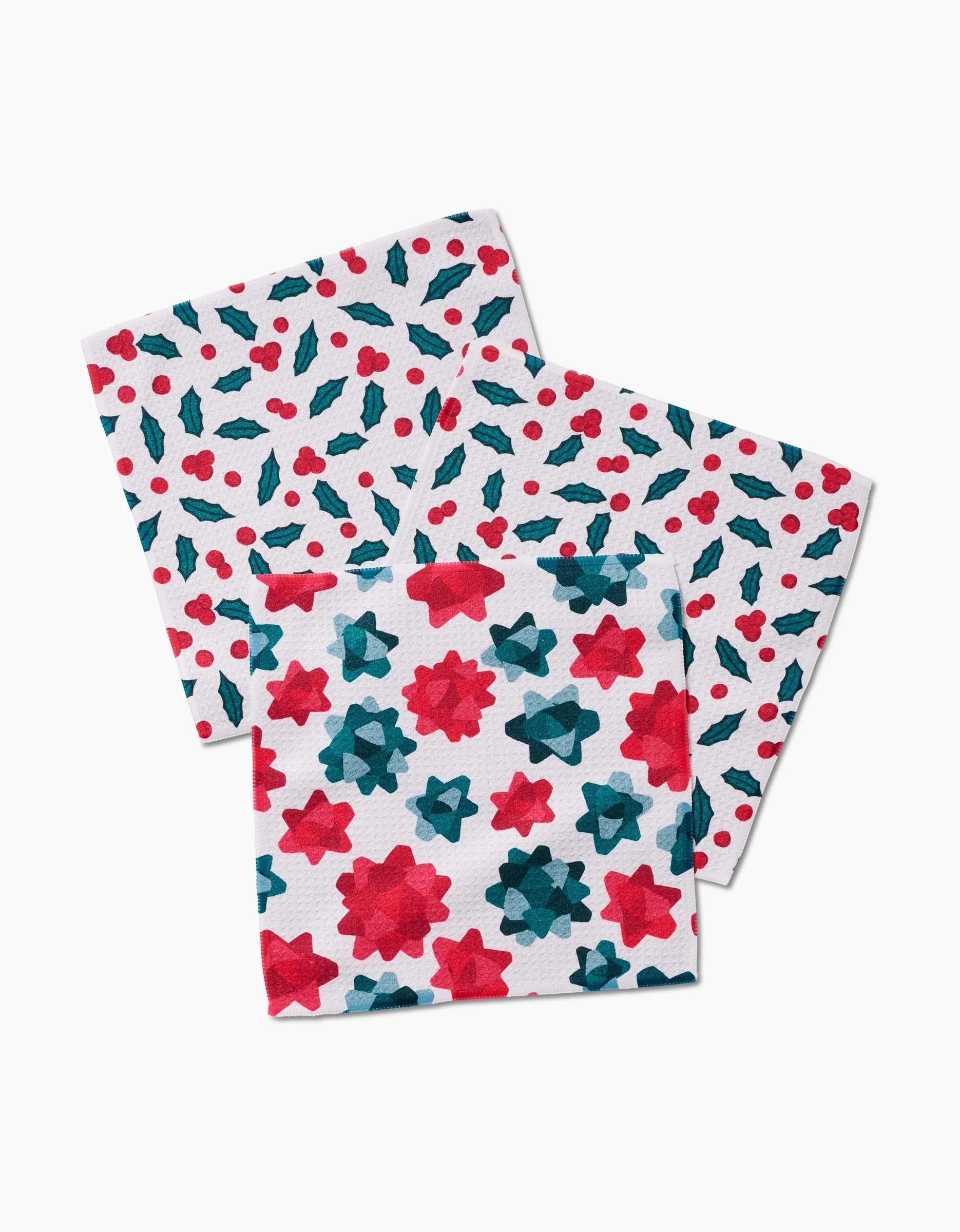 Three “Christmas Bows” napkins by Rebecca Bobko on a white background, made from recycled materials: two with red and green holly and berries, one with red and green star-like flower shapes.