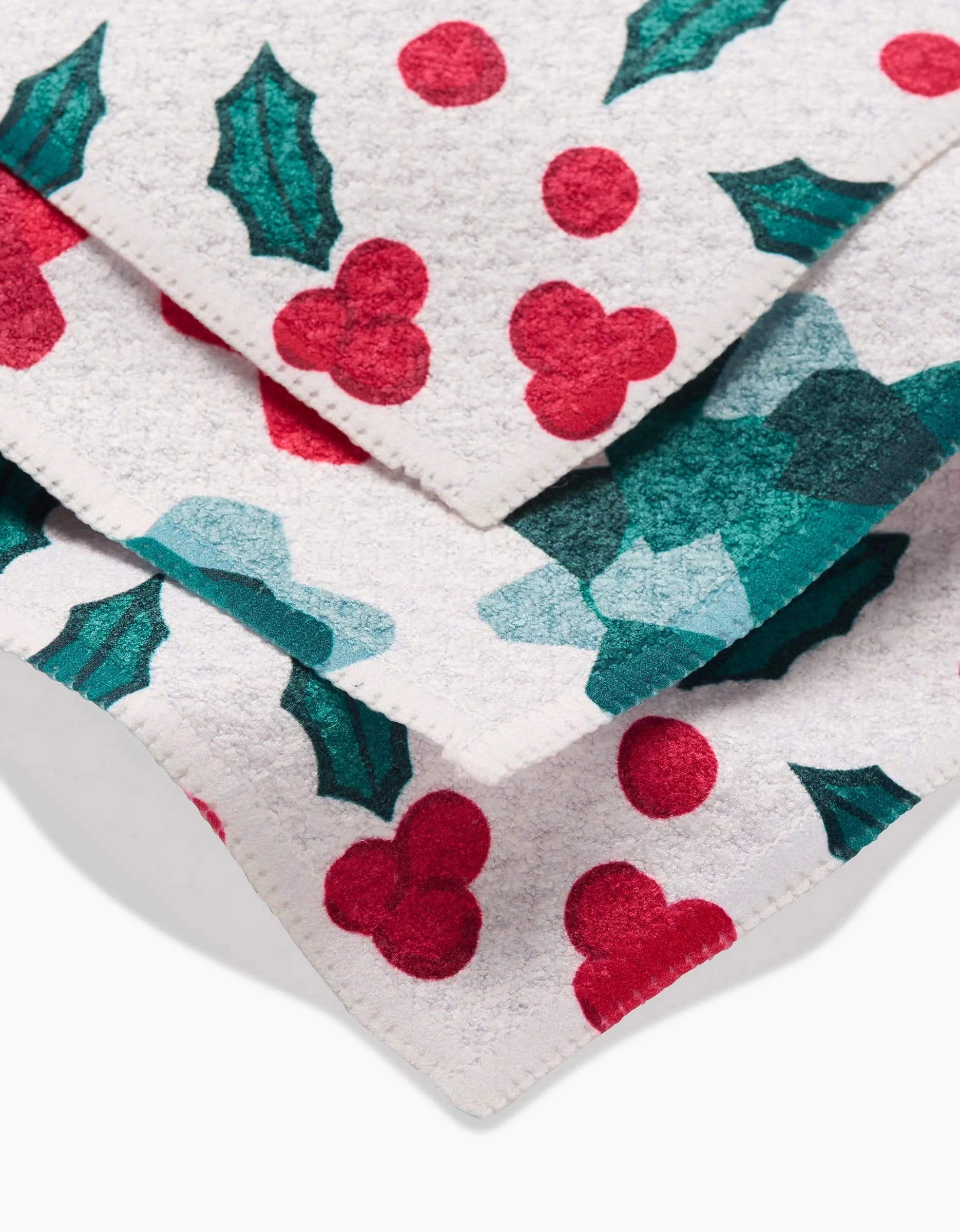 Close-up of festive Rebecca Bobko Christmas Bows layered on a white background, featuring red berries and green holly leaves. Made from recycled materials for an eco-friendly touch.