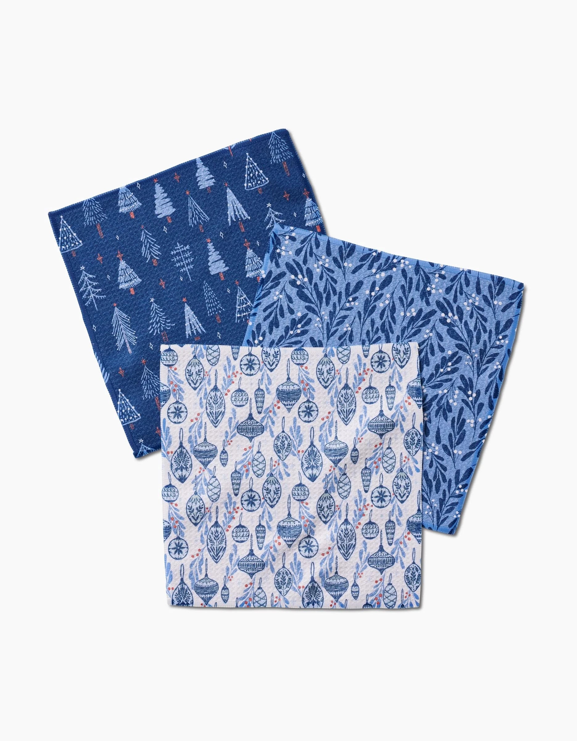 Set of three Hufton Studio Christmas Decorations Geoweave dishcloths: white and blue trees on dark blue, blue foliage on light blue, and blue ornaments with snowflakes on a white background.
