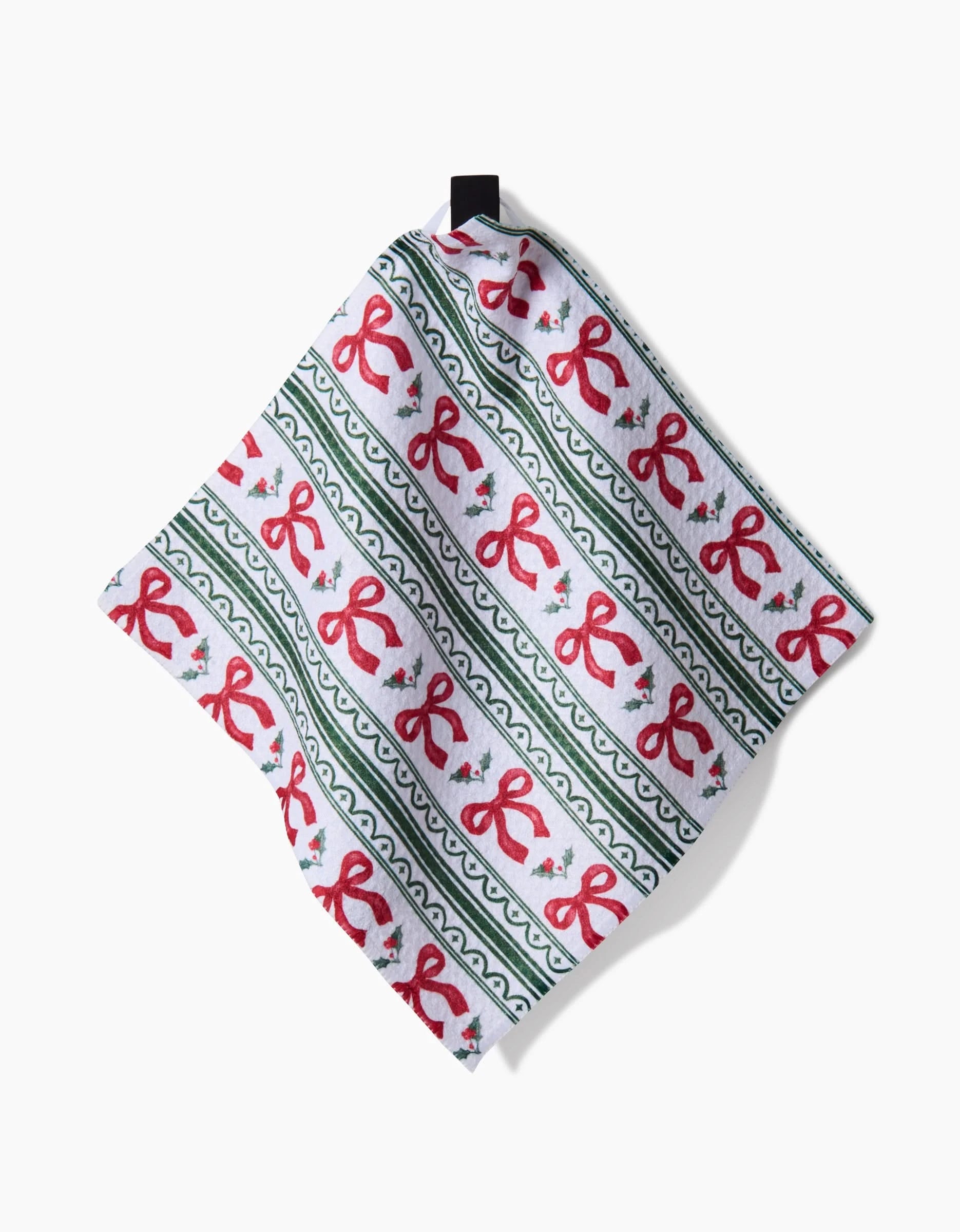 The Aubrey Fairchild Christmas Ribbons napkin is a square cloth made from Geoweave fabric, featuring red bows, green stripes, and holly leaves on white, displayed against a plain white background.