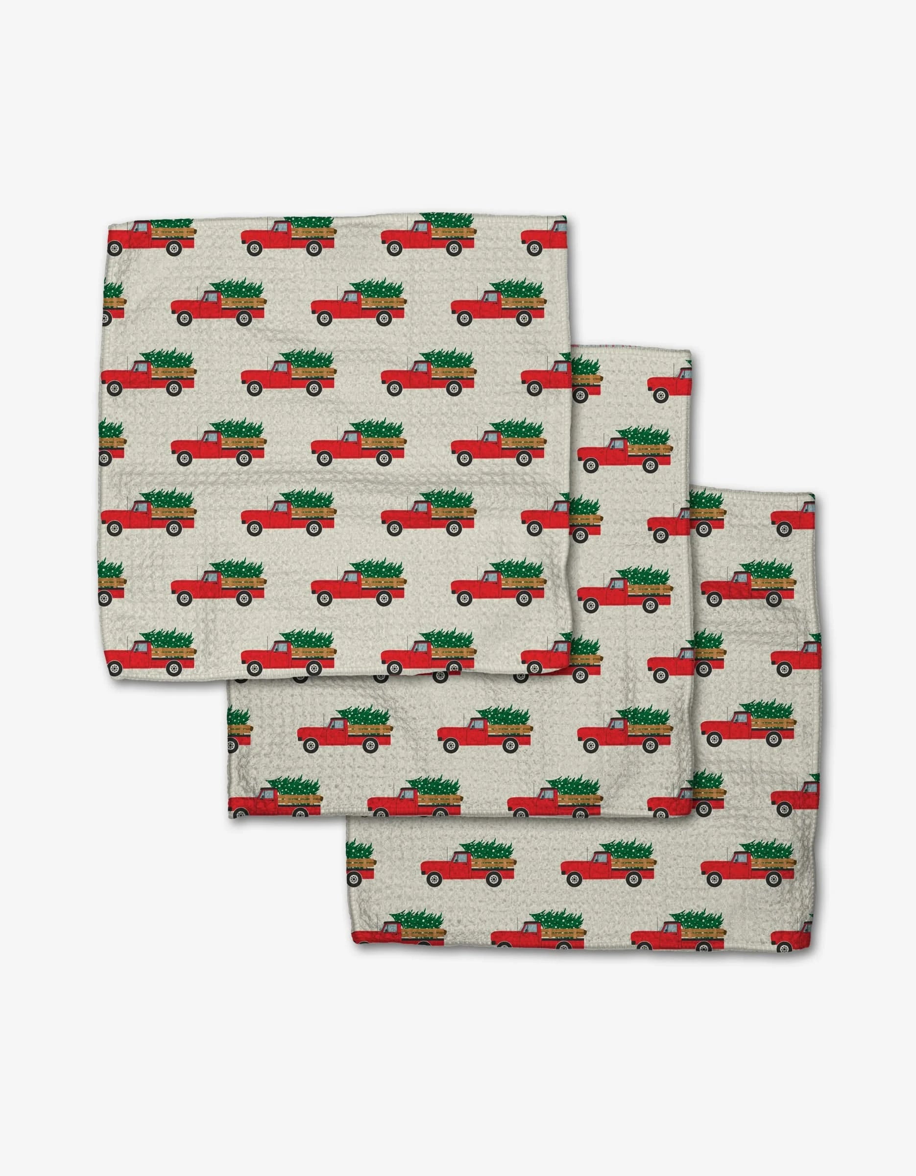 The Megan Kampa Christmas Ride set includes three beige Geoweave fabric napkins adorned with a repeating red vintage truck and green Christmas tree pattern, neatly stacked against a white background.