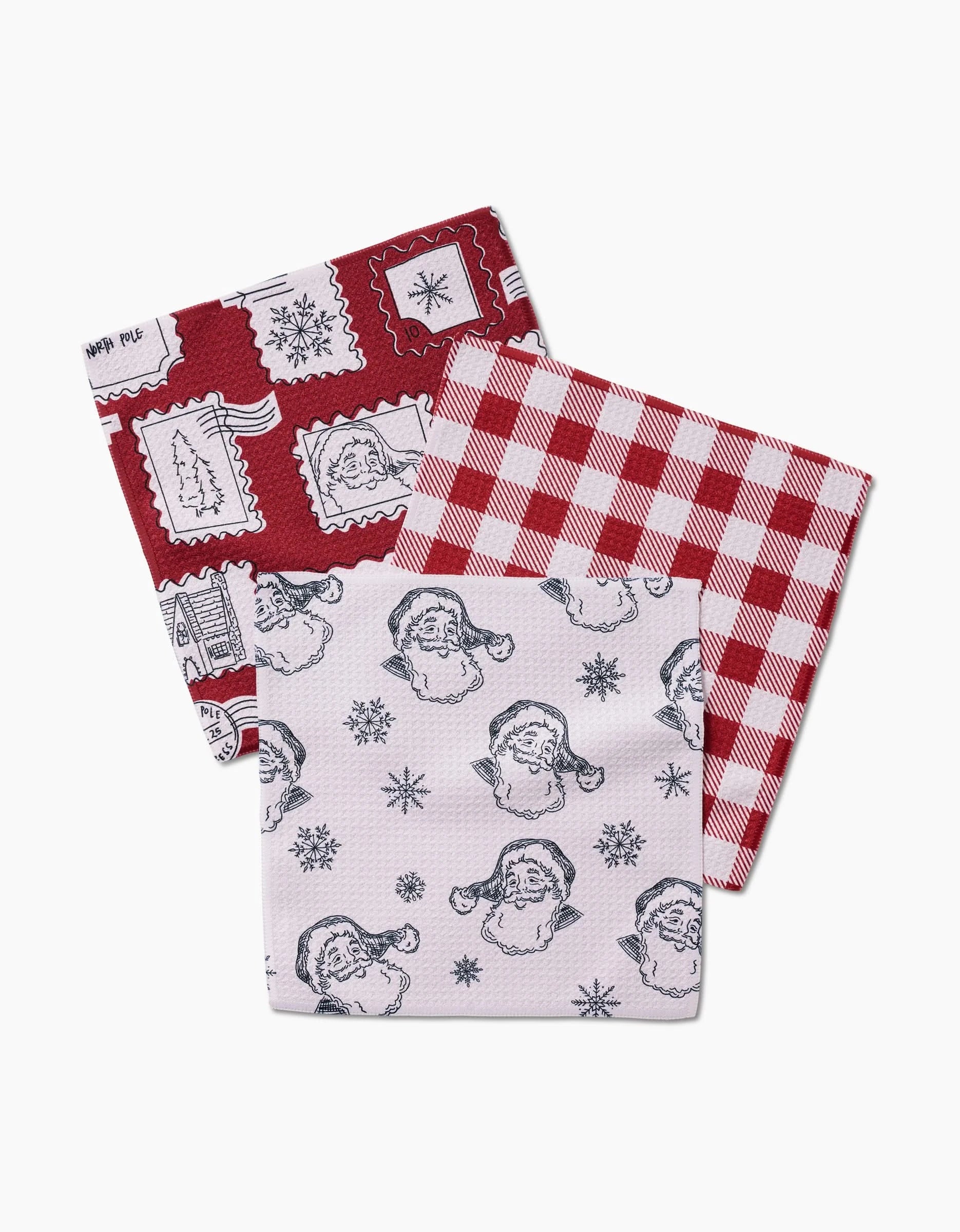 The Aubrey Fairchild Christmas Santa set includes three Geoweave cloth napkins: one with red holiday stamps, another with red and white gingham, and a third with black Santa faces and snowflakes on white.
