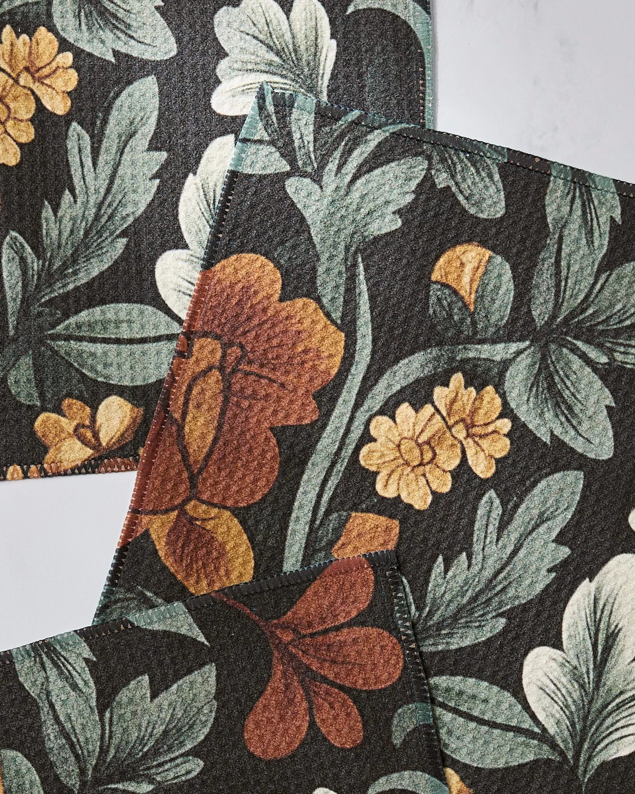 The Geometry Classic Floral set includes three fabric pieces made from recycled materials, featuring a dark background decorated with large green leaves and vivid orange, yellow, and red flowers overlapping on white.