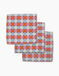 The Claire Iglesias Color Block Grid dishcloth set features three folded, checkered blankets in red, pink, blue, and white. Overlapping on a white background, they highlight fast-drying and super-absorbent qualities—perfect for any kitchen.