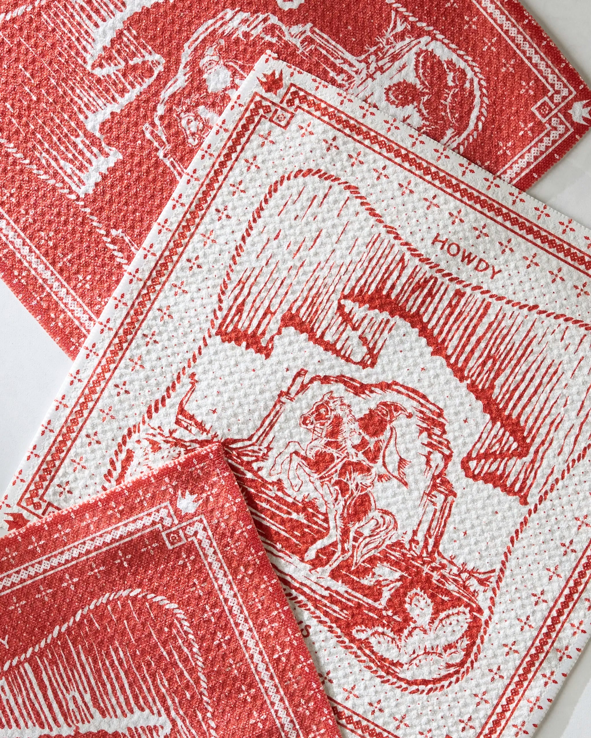 Geometry’s Cowboy Christmas dishcloth set features red and white Western-themed patterns with horses, riders, and “HOWDY” prints—perfect for adding festive fun to your kitchen.