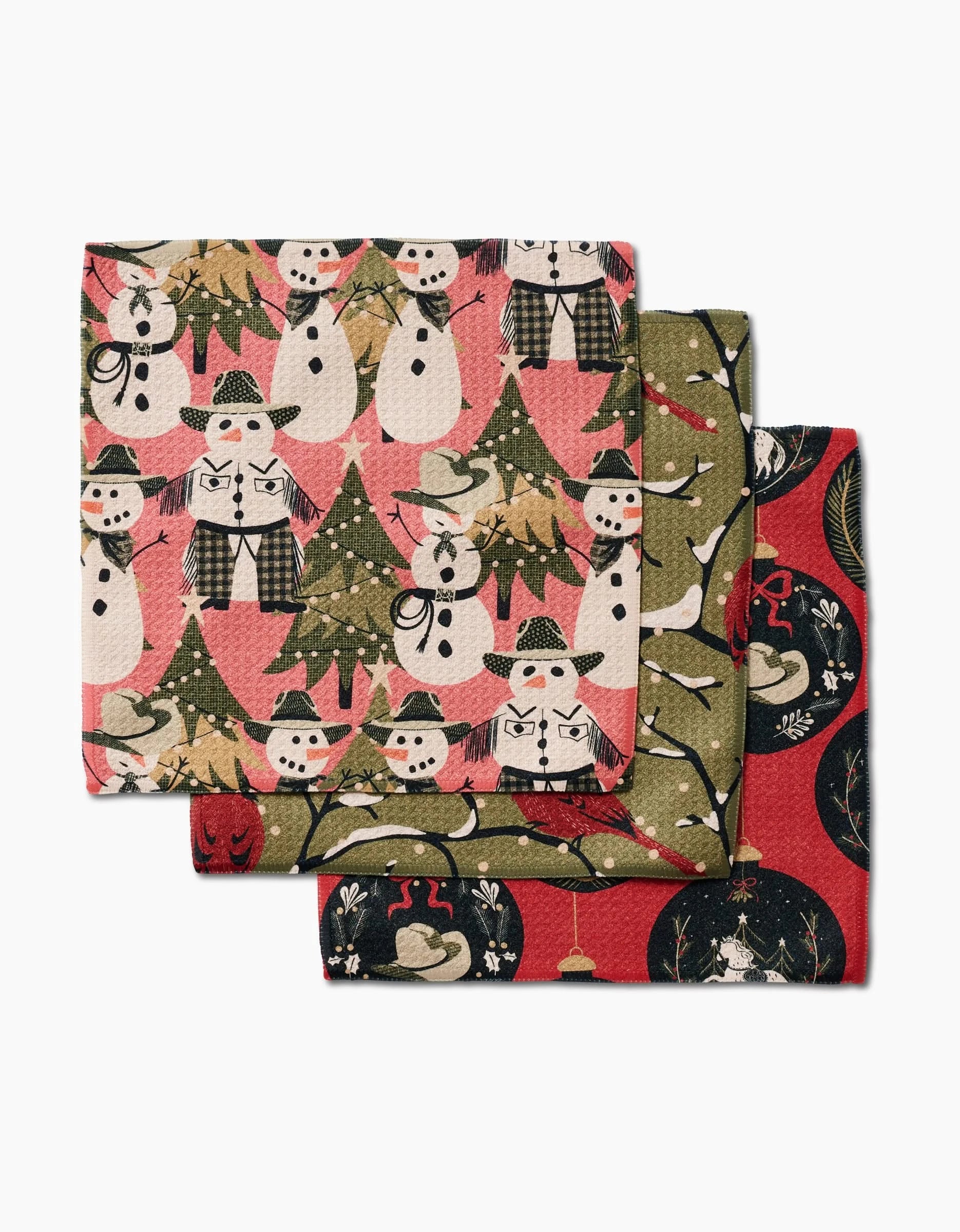 Cowboy Winter by Julianne Haness: a set of three Geoweave dishcloths with holiday designs—snowmen and trees on pink, snowmen on green, and woodland scenes on red and black backgrounds.
