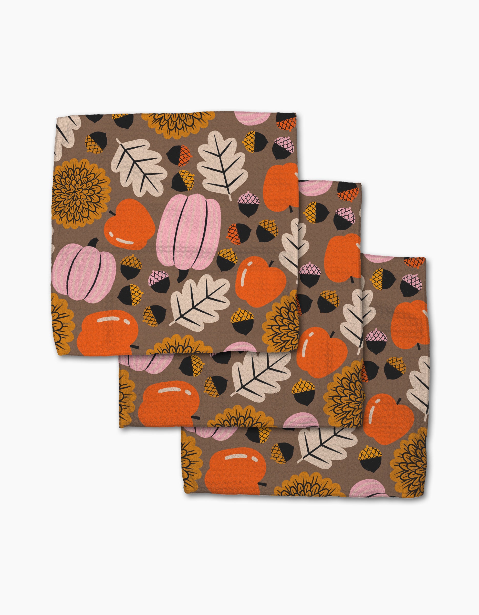 The Megan Roy "Crisp and Cozy" set includes three folded recycled kitchen cloths with autumn-themed patterns of orange and pink pumpkins, acorns, sunflowers, and fall leaves on a light brown background.