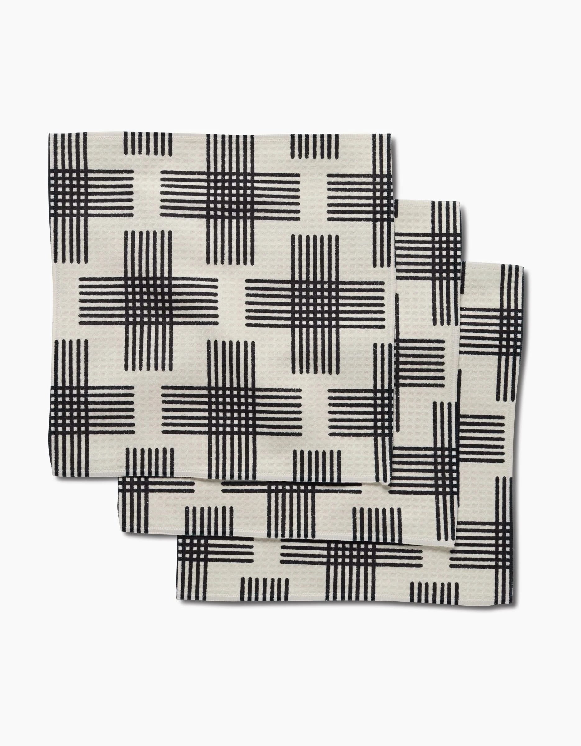 Three folded, cream-colored Cross Hatch napkins by Rosa Kichline, featuring a black crisscross grid pattern, are stacked slightly offset on a white background—these super-absorbent dishtowels use Geoweave fabric for superior cleaning.