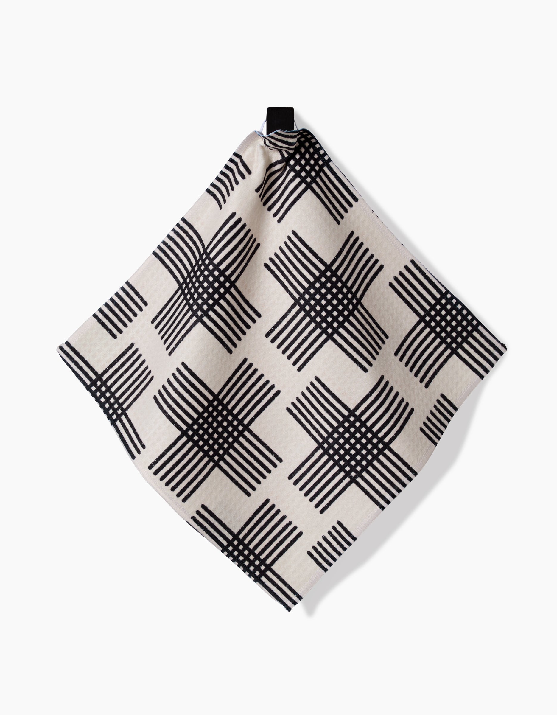 The Cross Hatch napkin by Rosa Kichline features a black geometric grid on beige Geoweave fabric and hangs from a black corner loop against a plain white background.