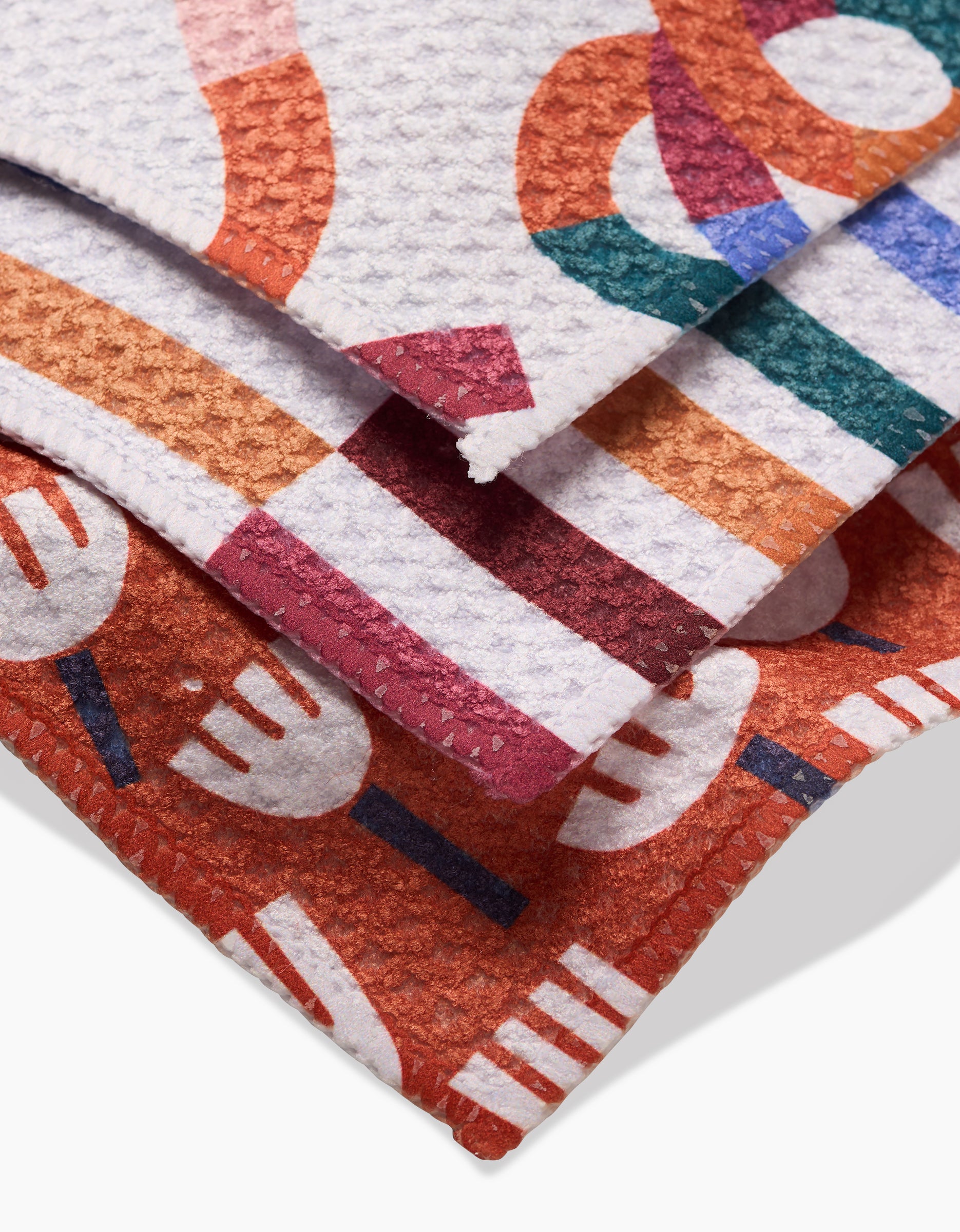 The Cutout Shapes Dishcloth Set by Claire Iglesias features three super-absorbent Geoweave cloths with colorful overlapping forks and abstract shapes in red, orange, green, and purple, neatly stacked on a white background.