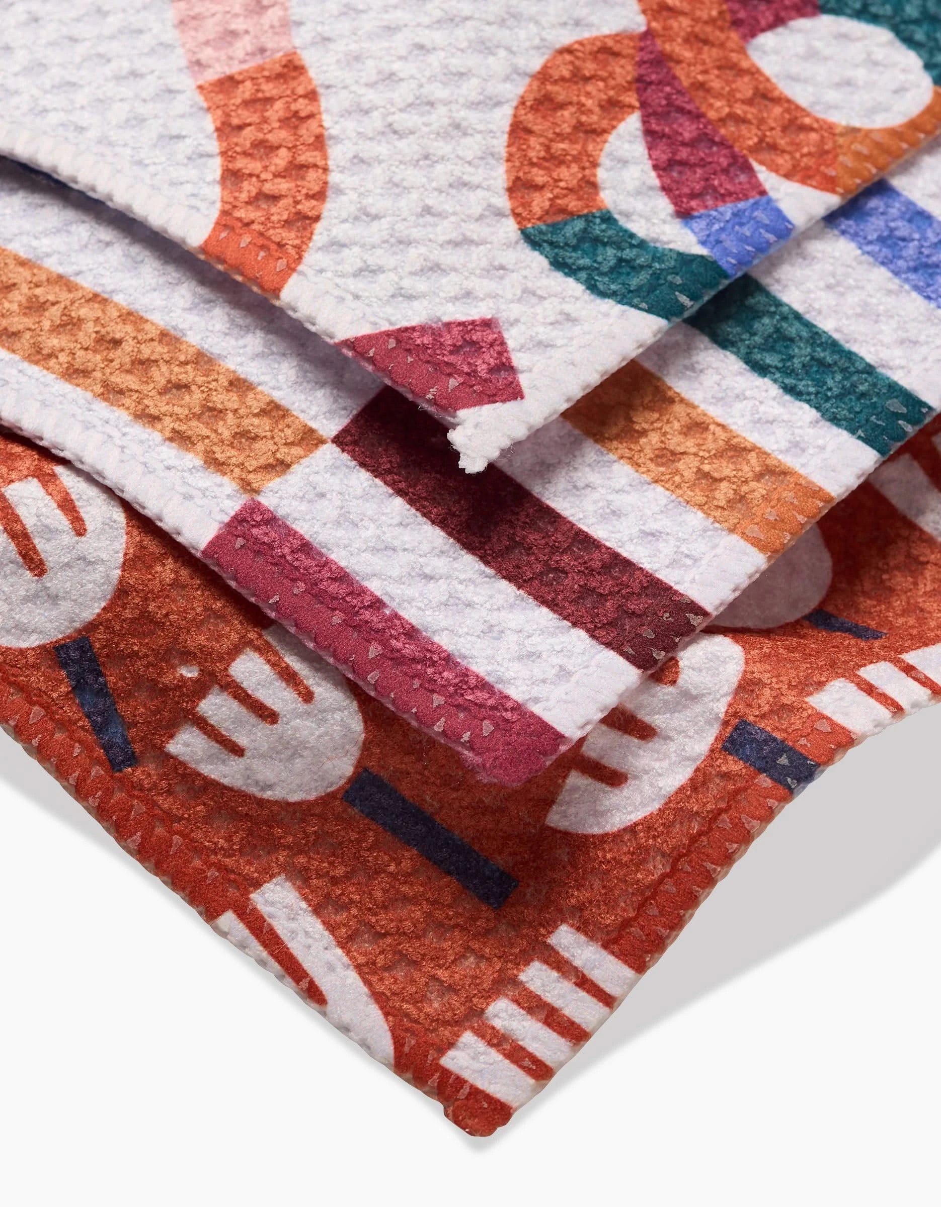 The Cutout Shapes Dishcloth Set by Claire Iglesias features three super-absorbent Geoweave cloths with colorful overlapping forks and abstract shapes in red, orange, green, and purple, neatly stacked on a white background.