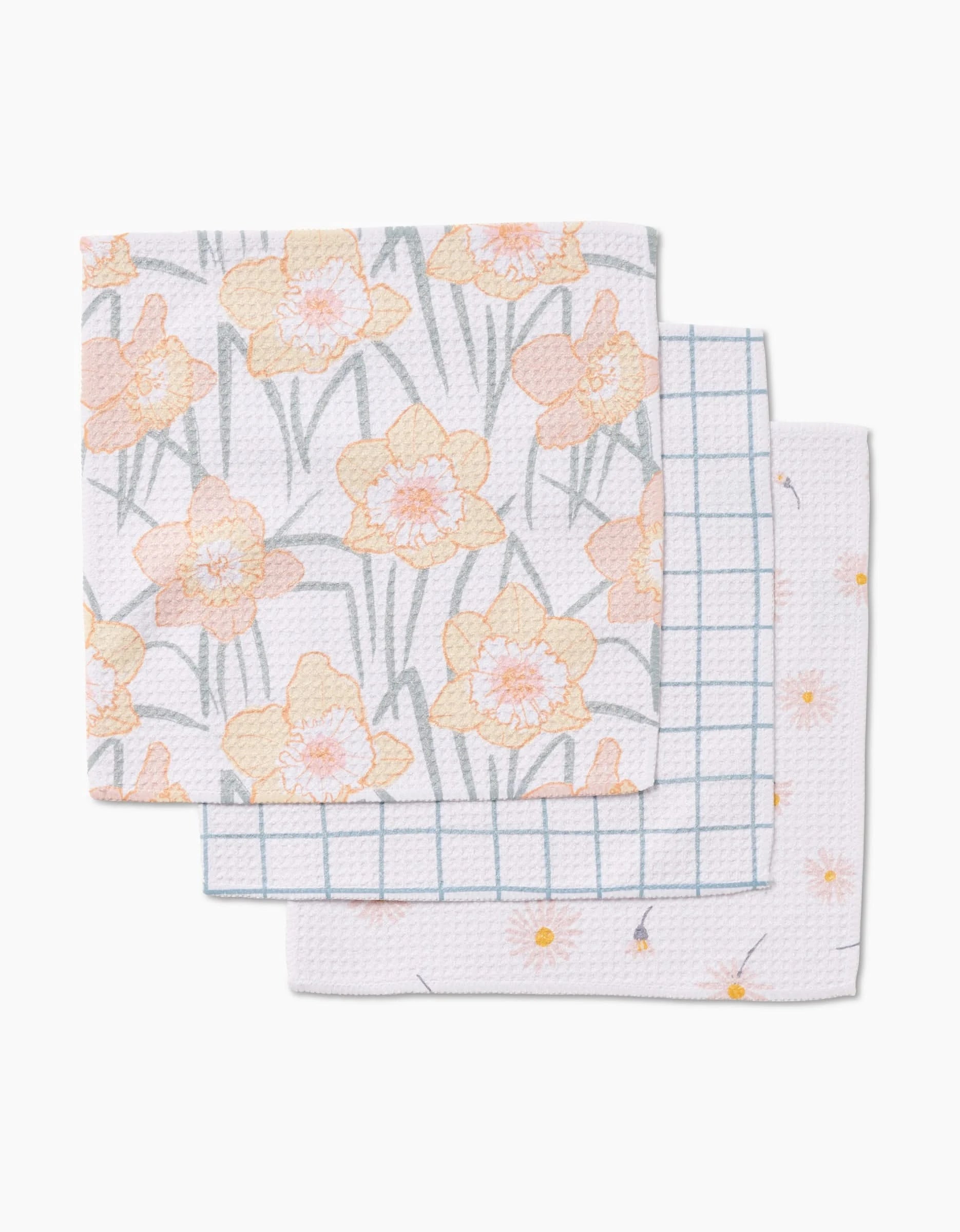 Three folded Hufton Studio Daisy Dust dishcloths are stacked: the top shows a yellow daffodil pattern, the middle a blue grid, and the bottom small yellow flowers—all made from super-absorbent Geoweave fabric.