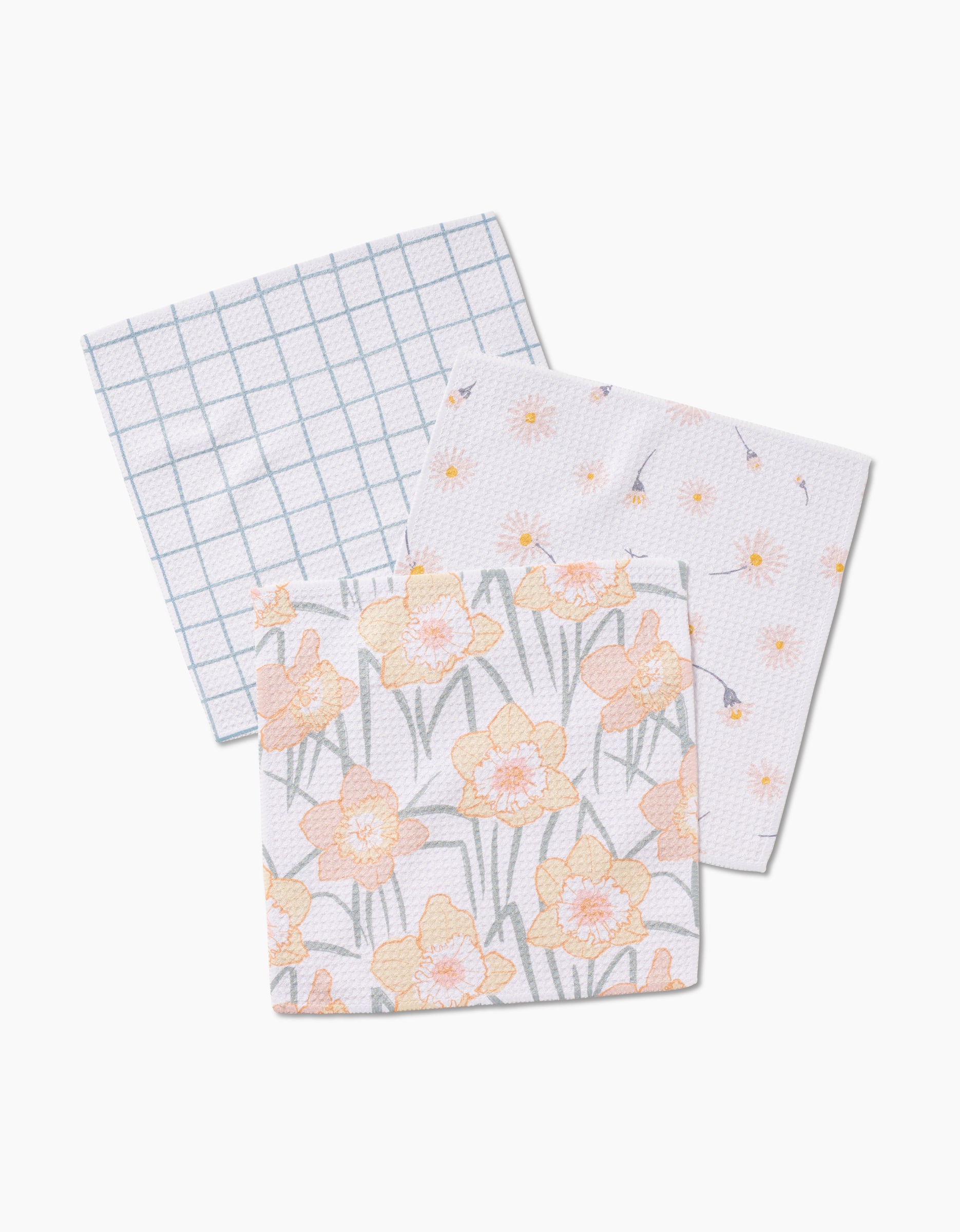 The Hufton Studio Daisy Dust set includes three square dishcloths: one with a blue grid, one with small yellow flowers, and one with large yellow daffodils on white, all crafted from super-absorbent Geoweave fabric.