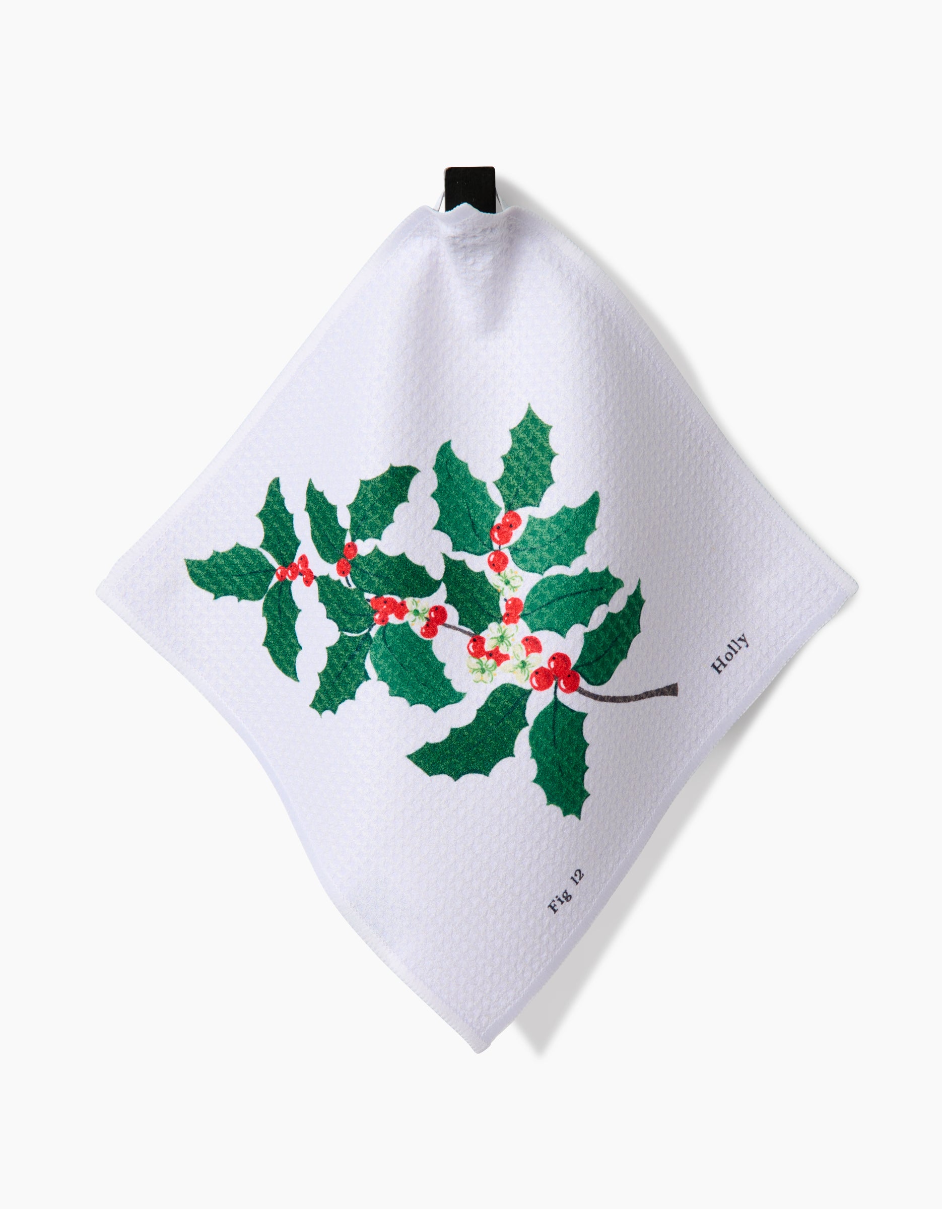 Linda Fox’s December Holly dishcloth features a green holly and red berries print on white Geoweave fabric, displayed with a black hanging loop.