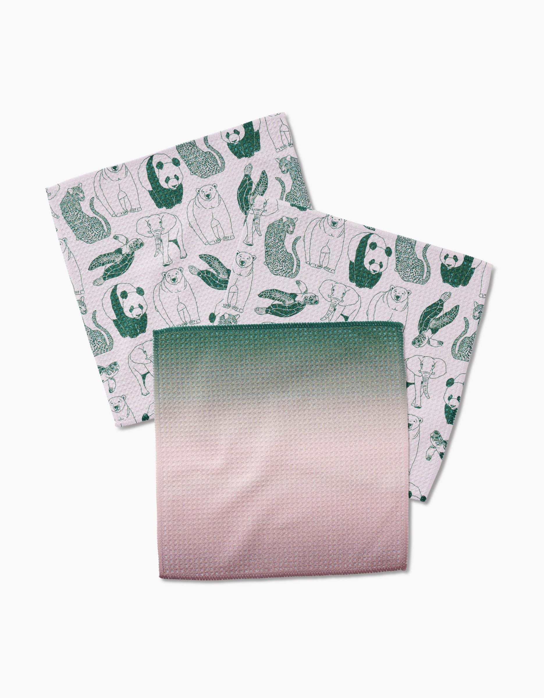 Three GEOMETRY Endangered Geoweave dishcloths—two with green animal prints on white (bears, otters, seals) and one in a green-to-pink gradient—are made from recycled materials and displayed on a white surface.