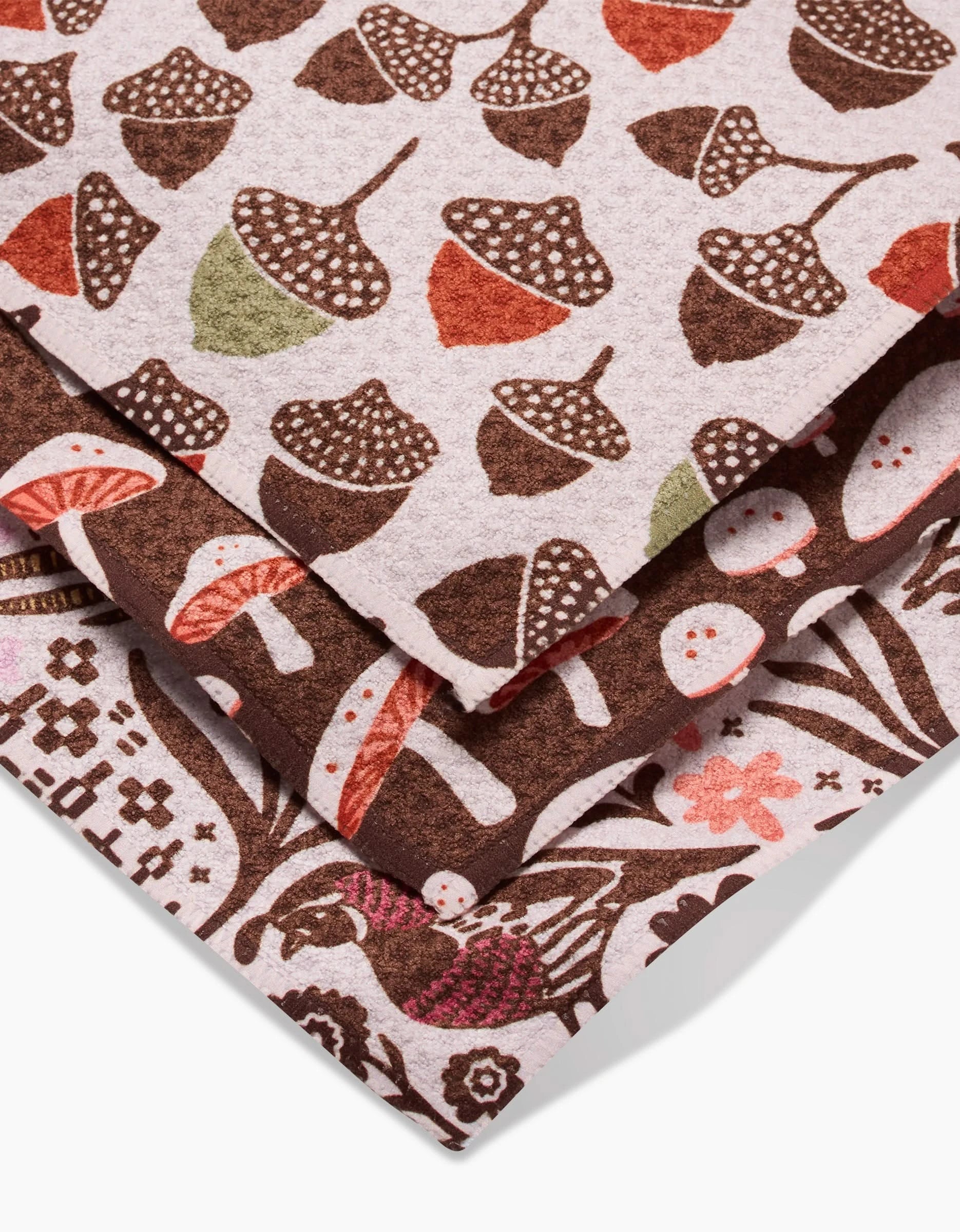 Kayla Ann’s Fall Abundance features three stacked Geoweave dishcloths with acorn, mushroom, and foliage patterns in earthy browns, reds, greens, and cream—stylish and eco-friendly, made from recycled materials.