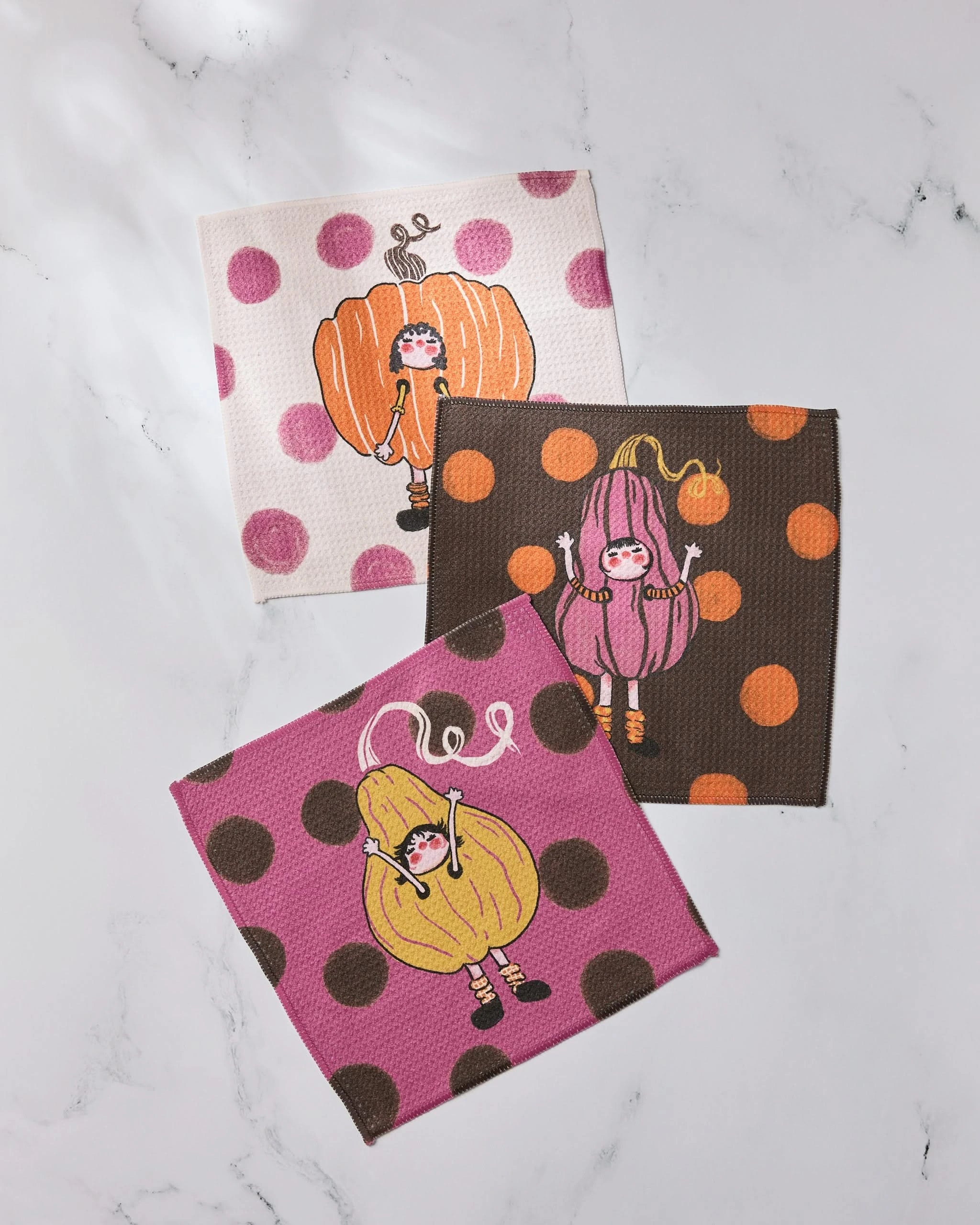 Geometry’s Fall Day Parade set includes three napkins with polka dot backgrounds, each featuring a girl in a colorful pumpkin costume—perfect on a white marble surface and ideal to pair with your favorite super-absorbent dishtowels.