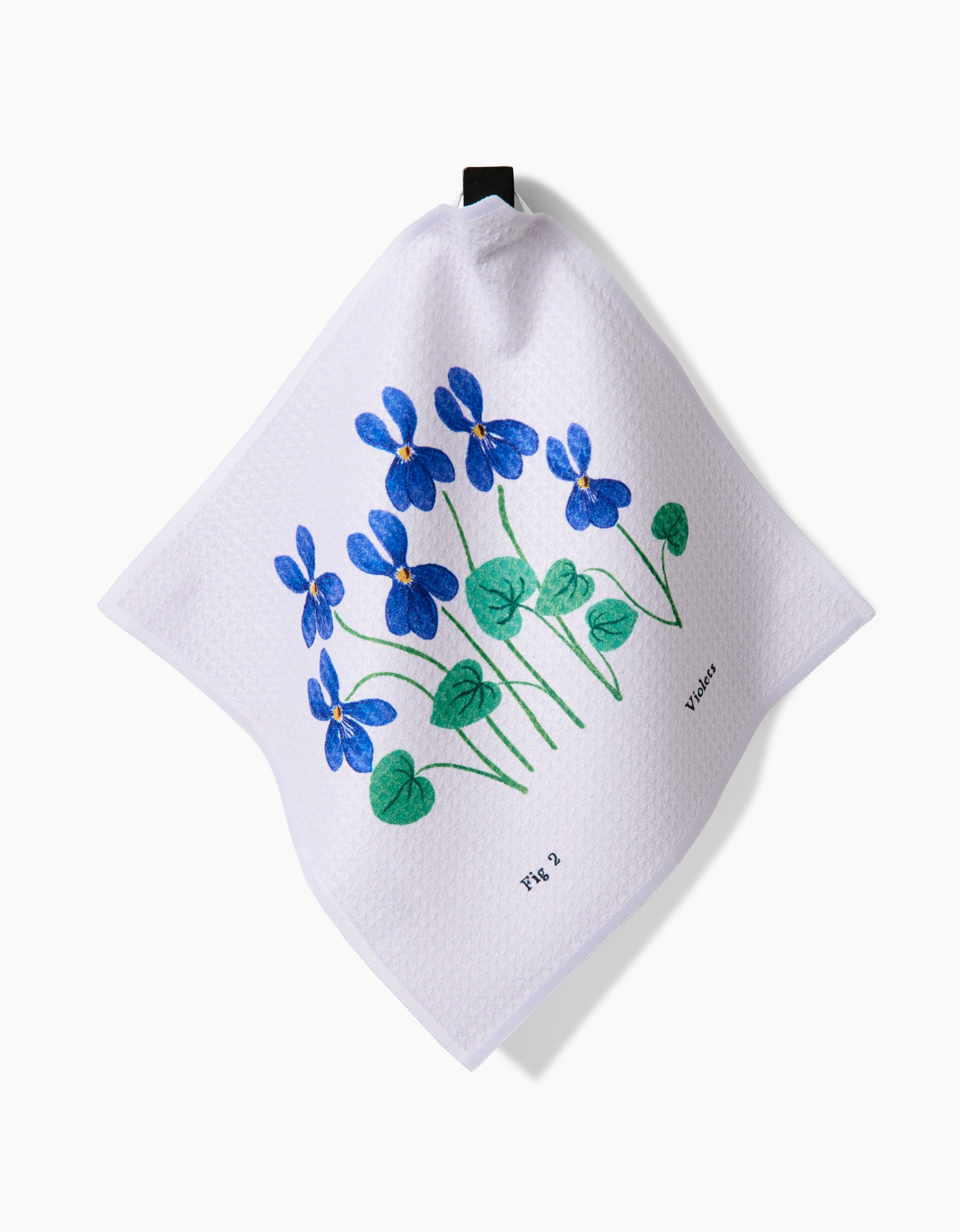 A white textured Geoweave cloth by Linda Fox, called February Violets, features blue and purple violet flowers with green leaves, black loop for hanging, and Fig 3 Violet text—part of a super-absorbent dishcloth set.
