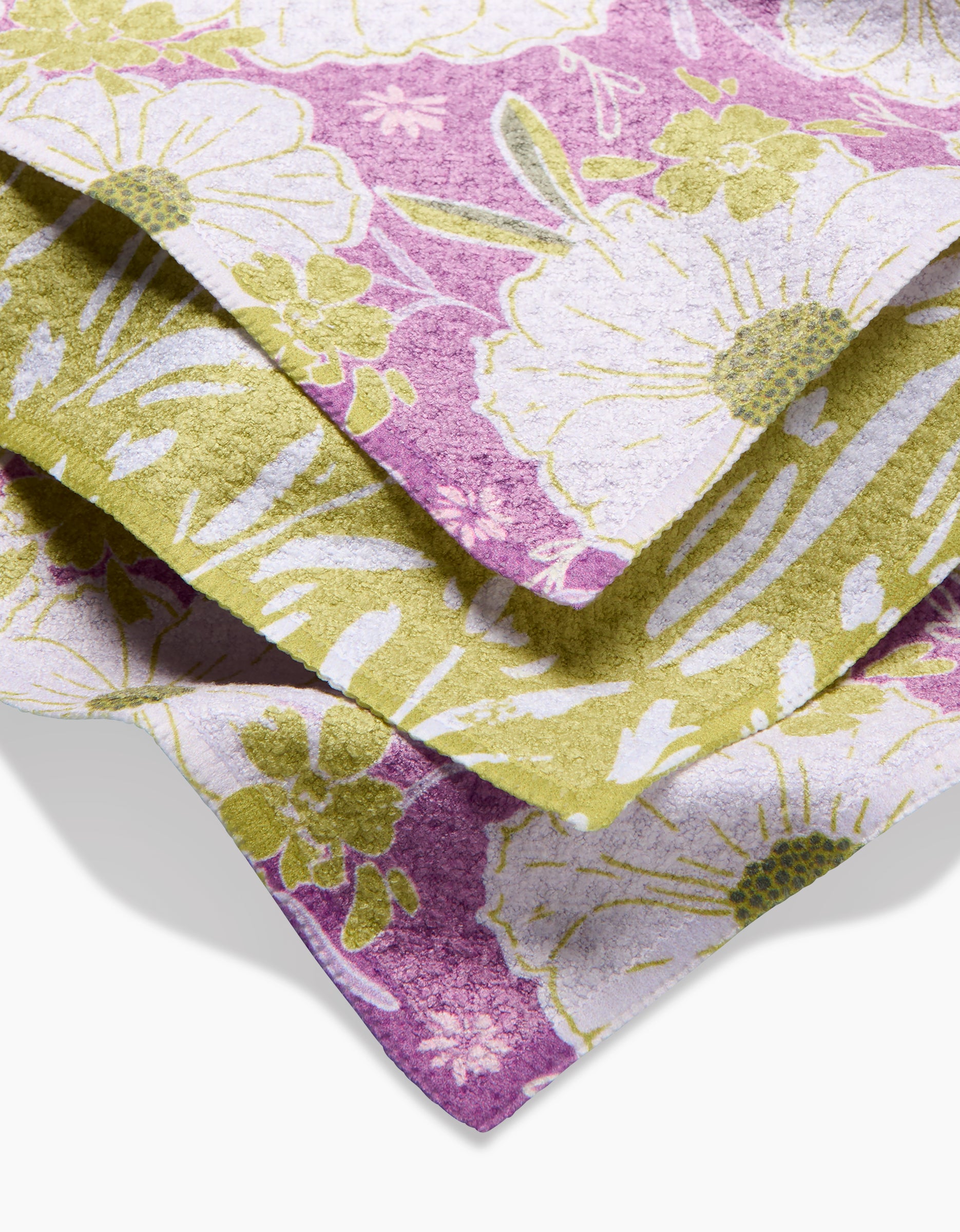 A close-up of folded Ashley Celena Field of Spring Flowers towels, featuring soft Geoweave fabric with a floral pattern in white, green, and purple tones and large flower and leafy details.