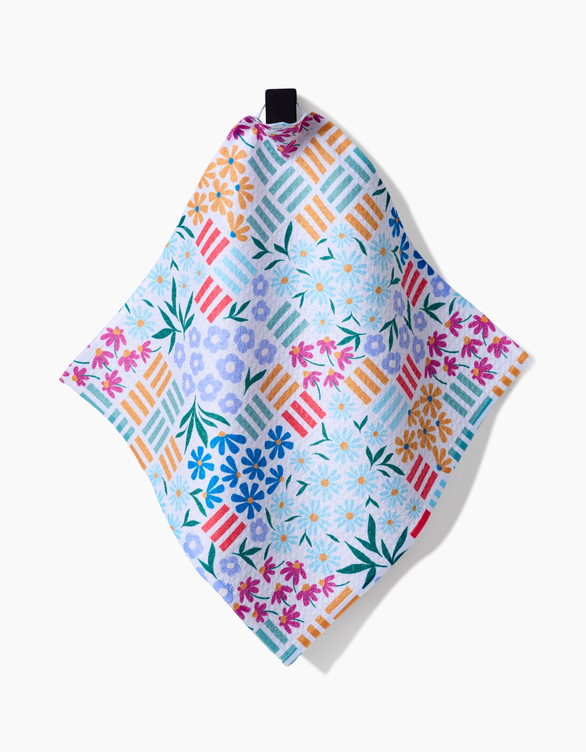 The Floral Garden dishcloth by Charlie Rowan Designs features recycled materials, a square shape, vibrant daisies and geometric patterns in blue, purple, and orange, and is topped with a black hanging loop.