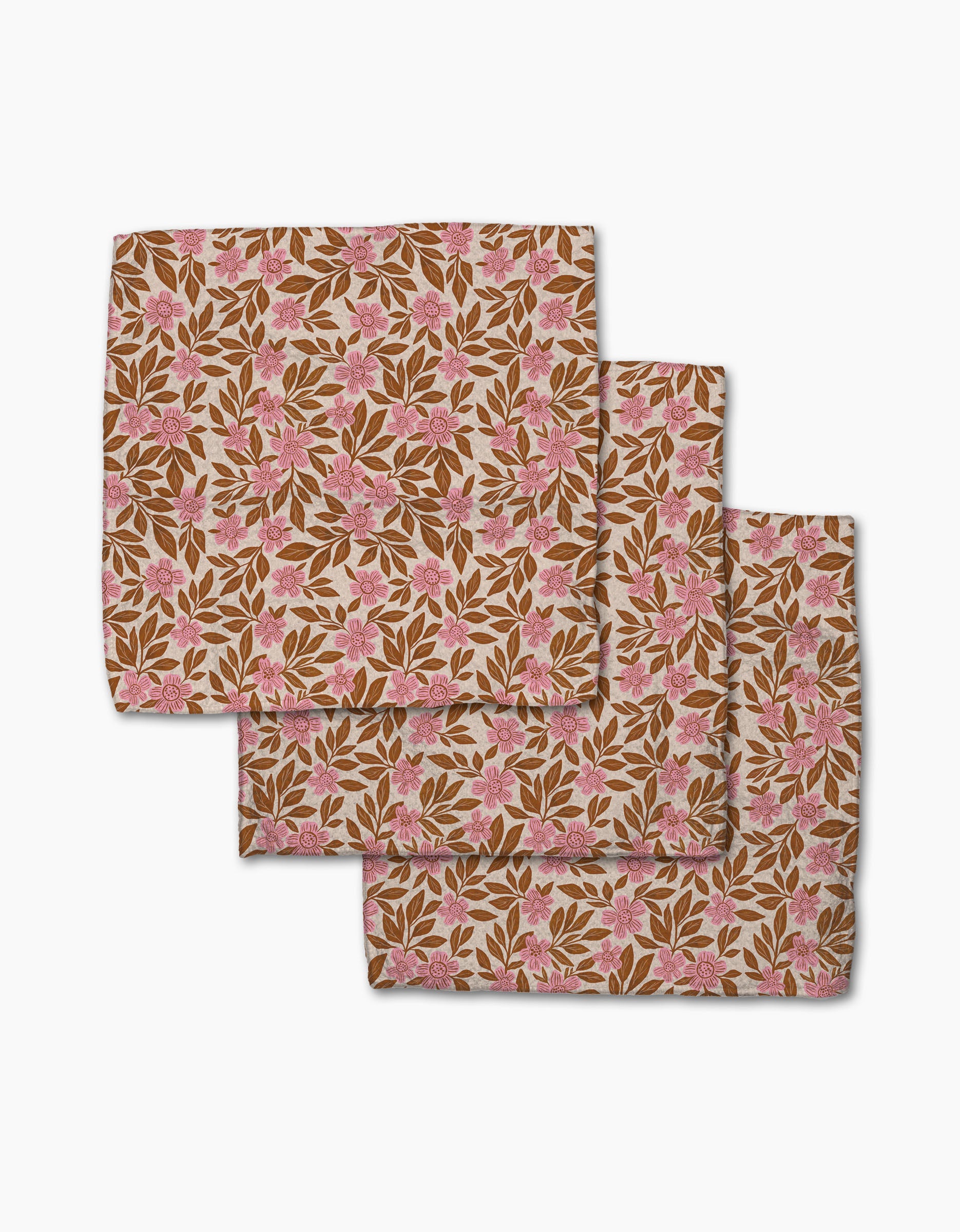 Three Floral Meadow square cloth napkins by Lisa Nelson, made from recycled materials, feature pink flowers and brown leaves on beige. They're shown overlapping on a white surface.