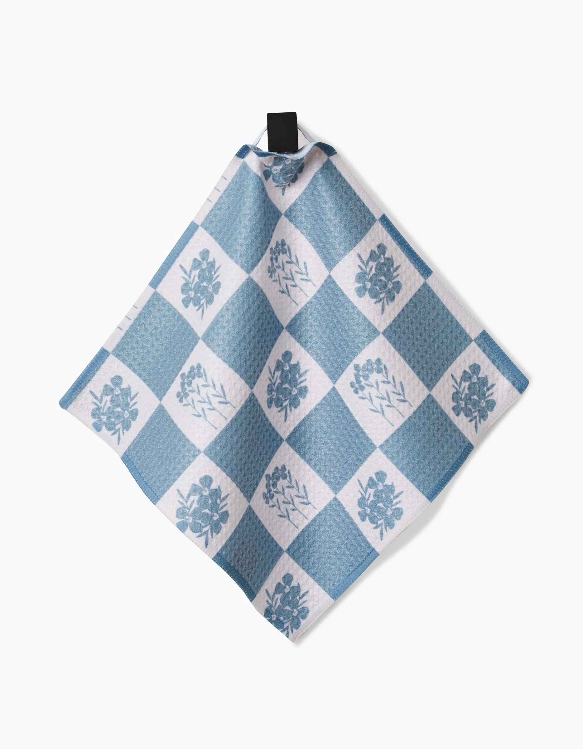 The Charlie Rowan Designs Floral Patchwork Geoweave dish towel features blue and white checkered fabric with floral and leaf motifs, hanging from a black loop against a white background.