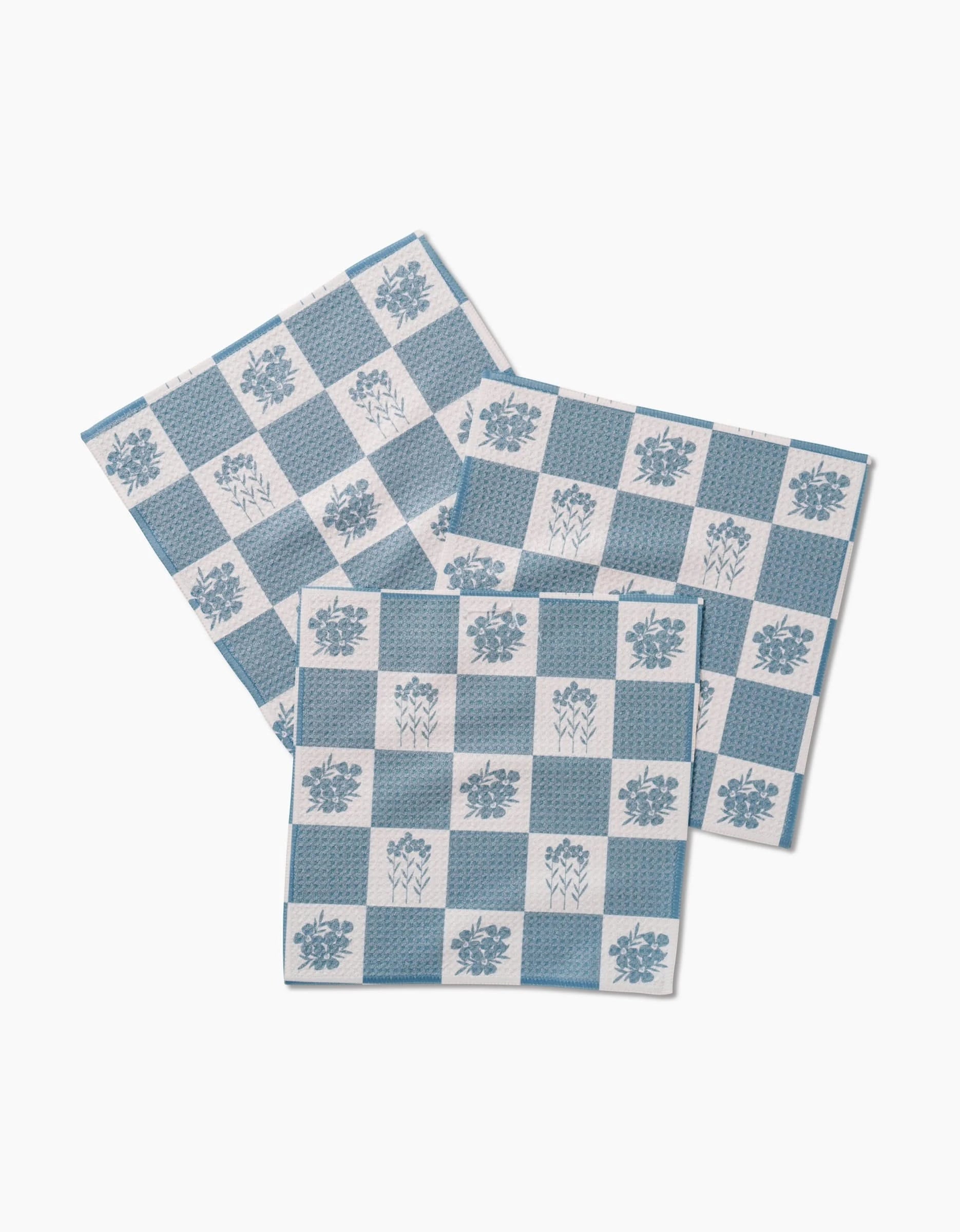 Three Floral Patchwork napkins by Charlie Rowan Designs, crafted from premium Geoweave fabric, feature blue and white checkered floral patterns and are arranged overlapping on a white background.