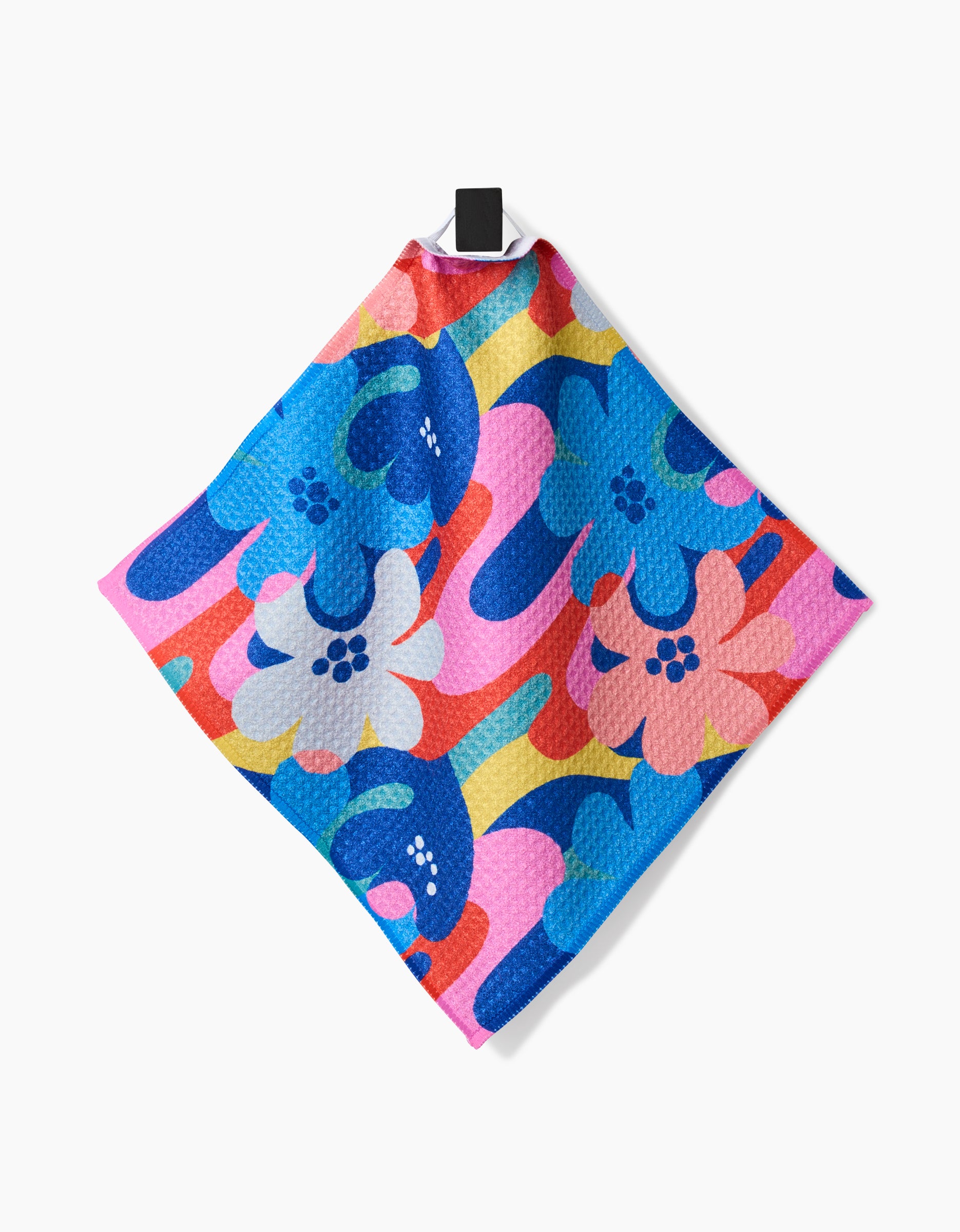 The Flower Powers dishcloth by Masha Volnova, made from Geoweave fabric and featuring a vibrant blue, pink, red, yellow, and white floral pattern, hangs on a black hook against a white background.