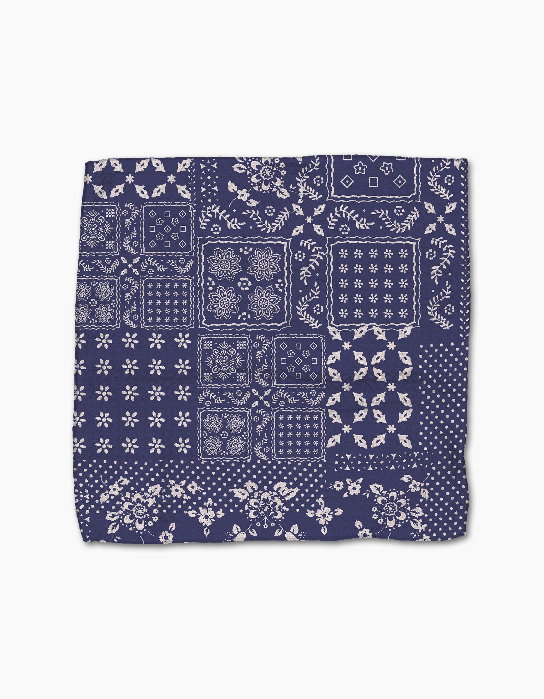 The Geometry Flowing Ocean bandana features a patchwork of white floral and geometric patterns on navy blue squares, made from soft Geoweave fabric. The background is white.