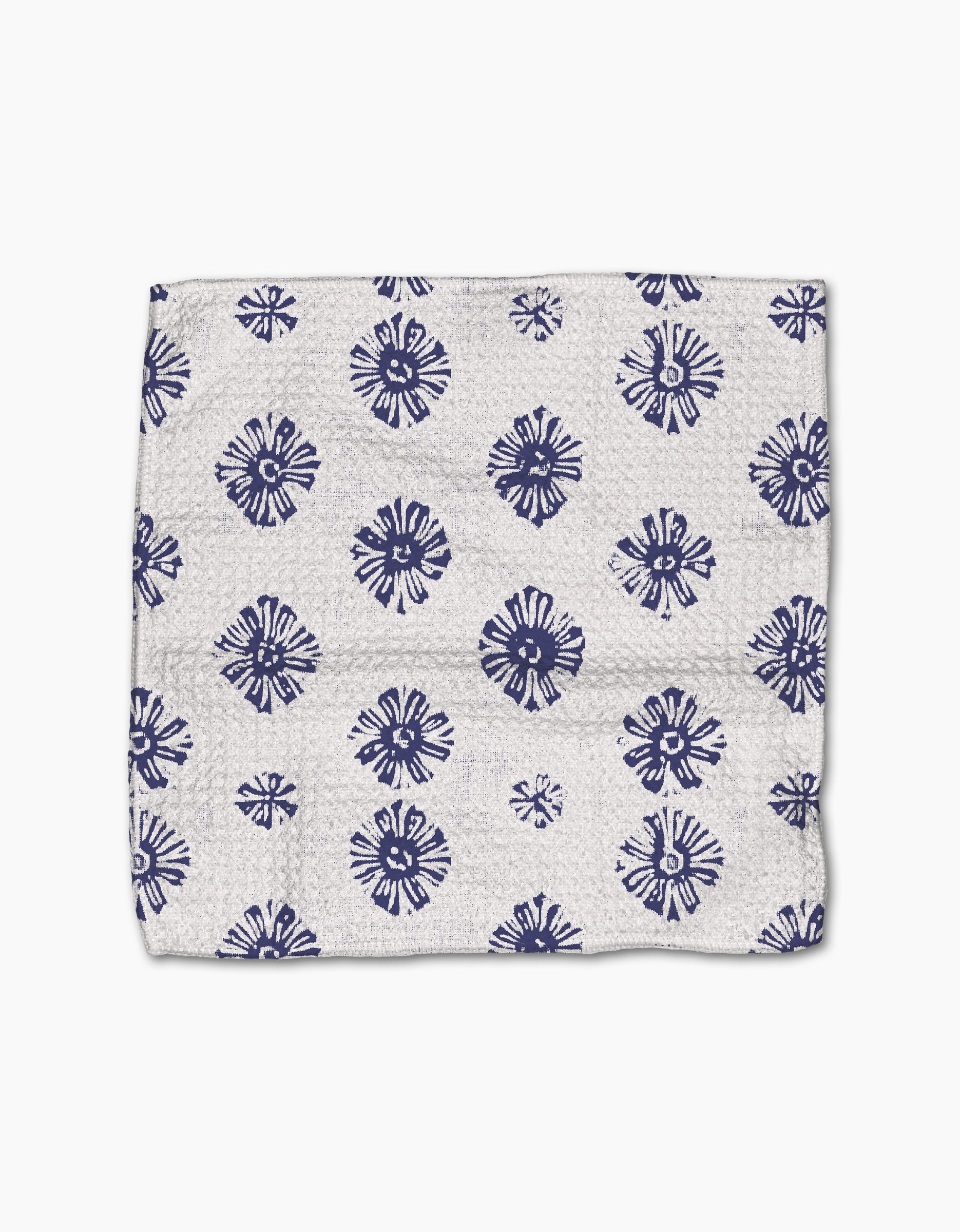 The Flowing Ocean dishtowel by Geometry is made of white Geoweave fabric with evenly spaced navy blue, circular, floral-like patterns. This super-absorbent towel is shown laid flat with gentle creases.