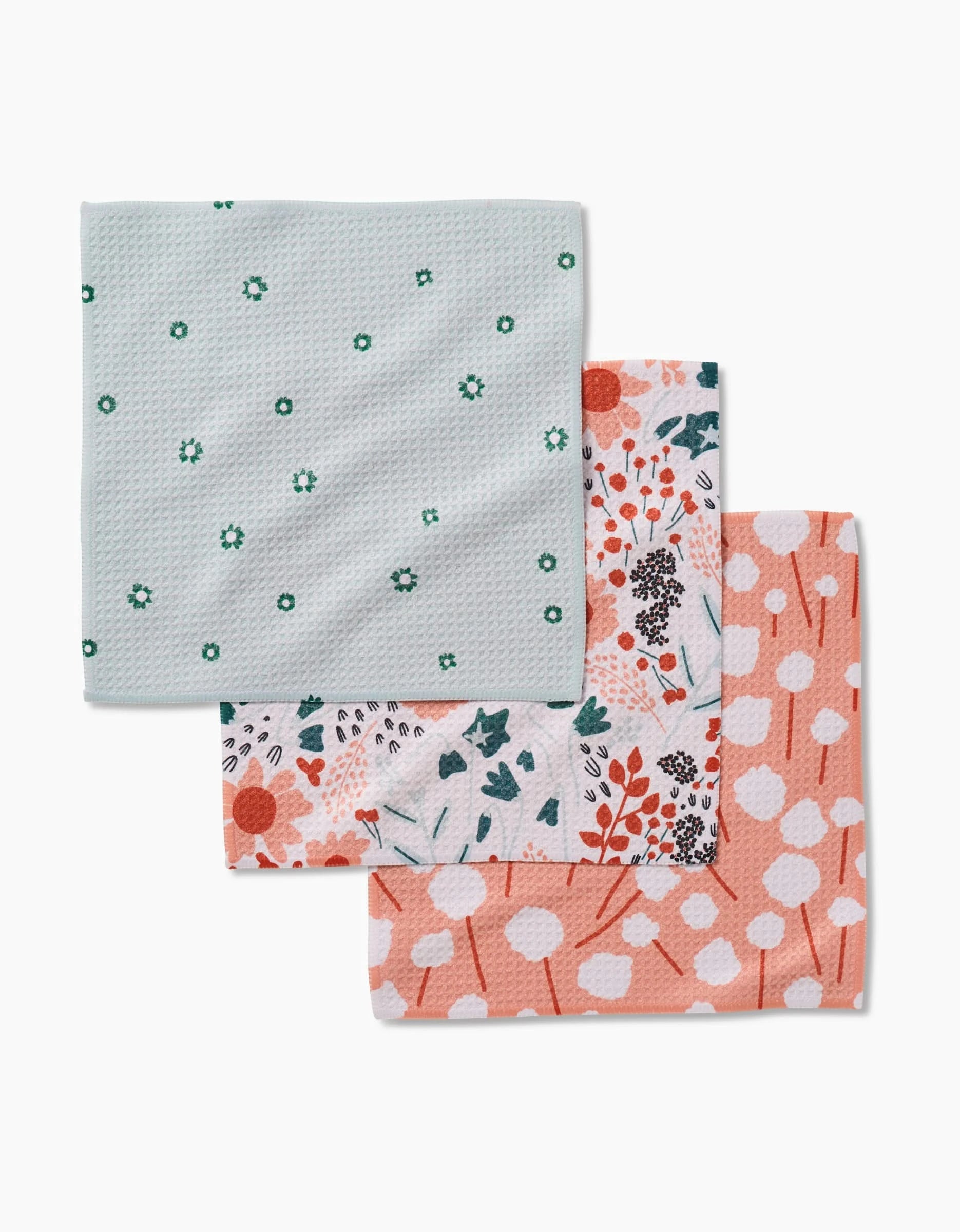 Coit Creative’s Forest Florals set includes three folded dishcloths made from recycled materials: light blue with green flowers, colorful floral print, and peach with white cotton spots.
