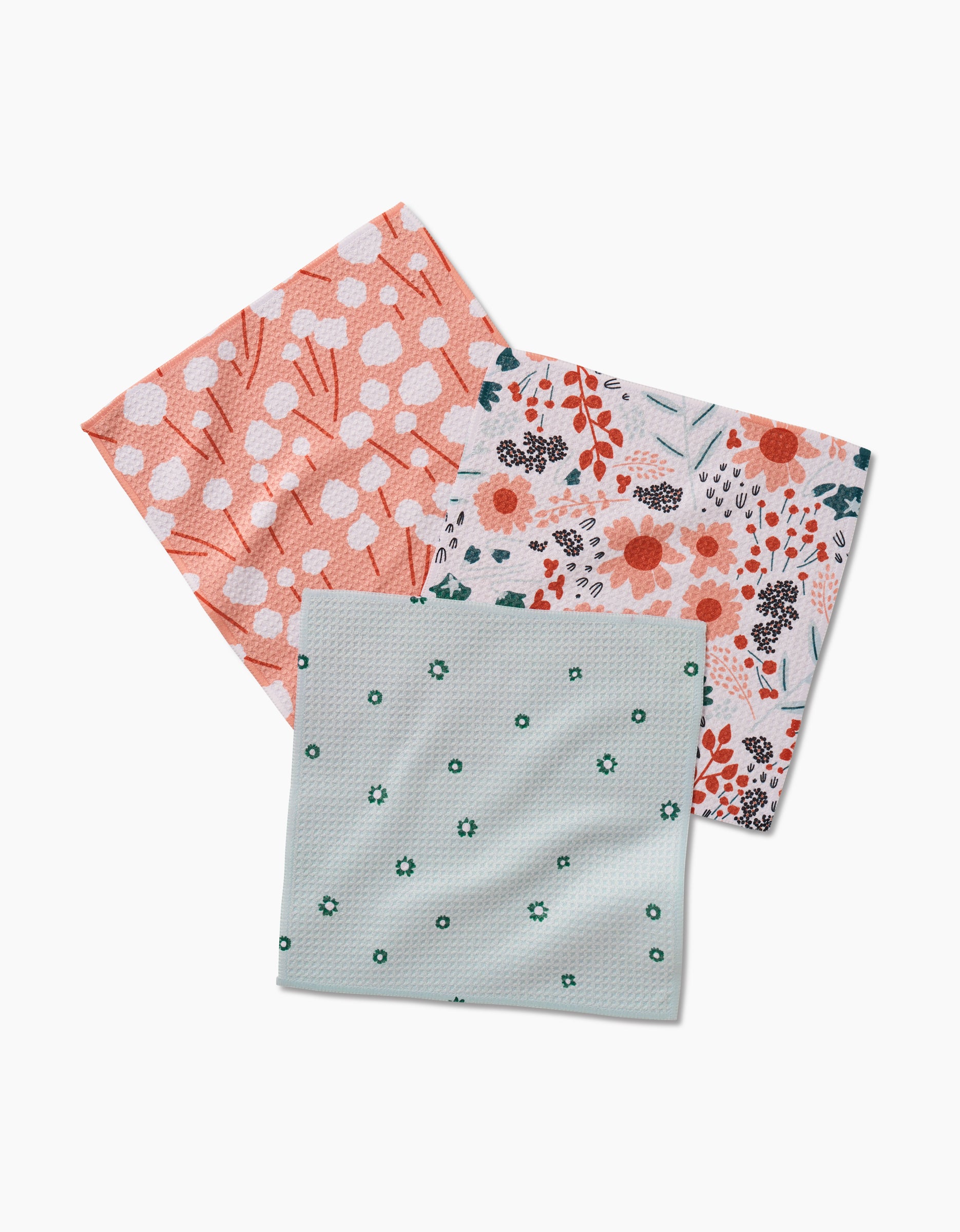 The Forest Florals set by Coit Creative includes three square dishcloths made from recycled materials: coral with white polka dots, multicolored florals, and light blue with small green flowers.