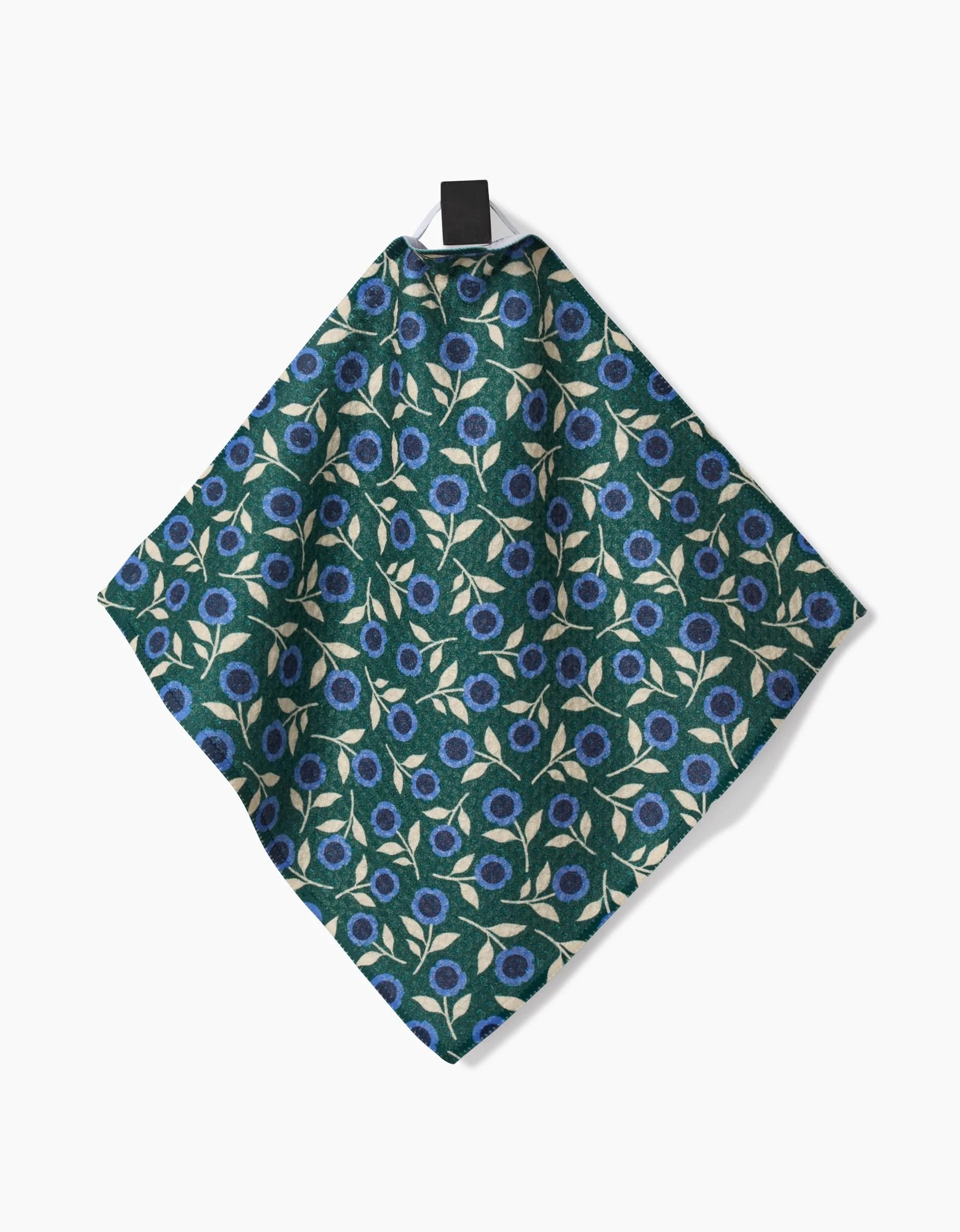 The Friendly Fleurs handkerchief by Megan Kampa, made from recycled materials, showcases blue and white flowers with beige leaves on green fabric. It hangs from a black clip against a white background.