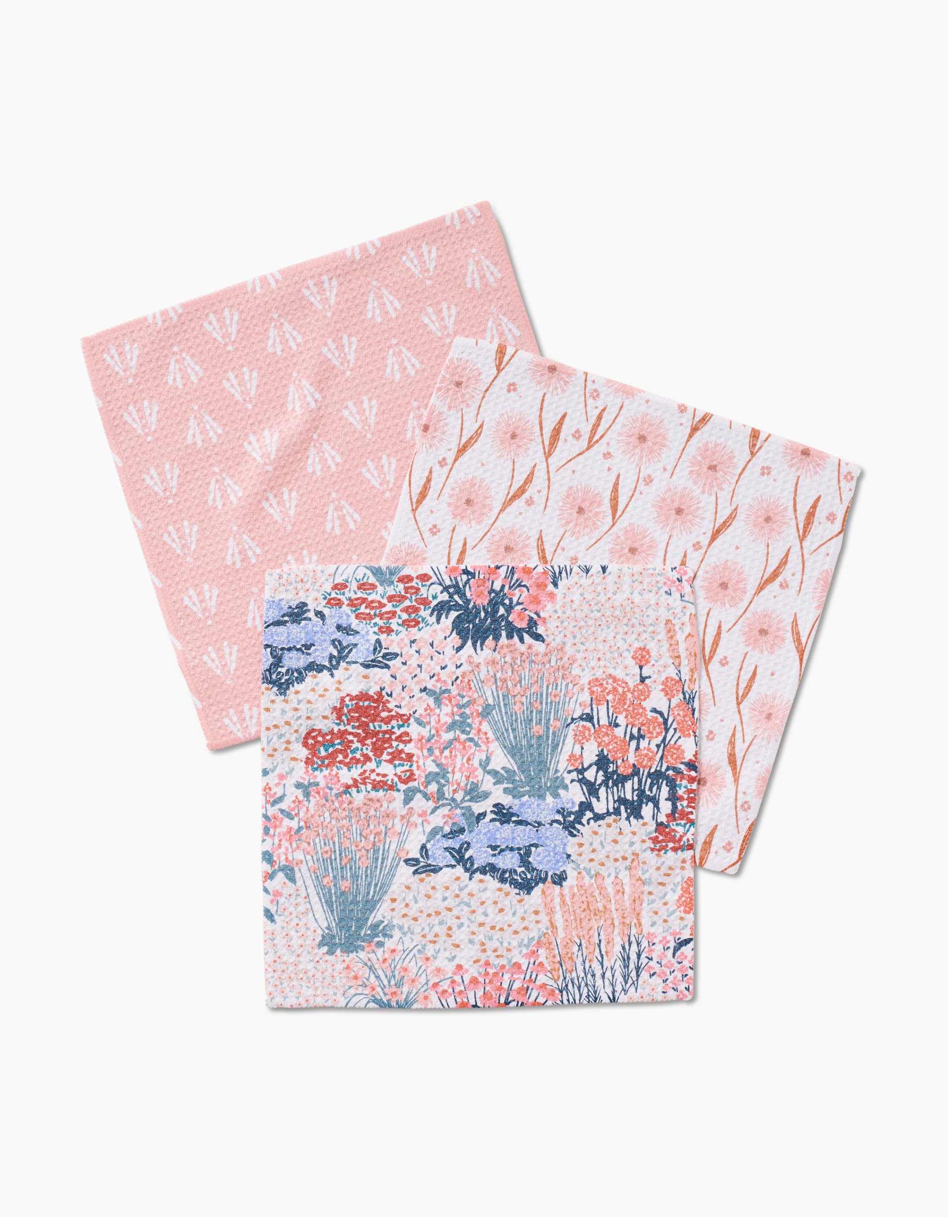 The Hufton Studio Garden Bloom set features three folded napkins: white abstract shapes on pink, pink flowers with wavy brown lines on white, and a dense blue, pink, and orange floral design—all made from recycled materials.