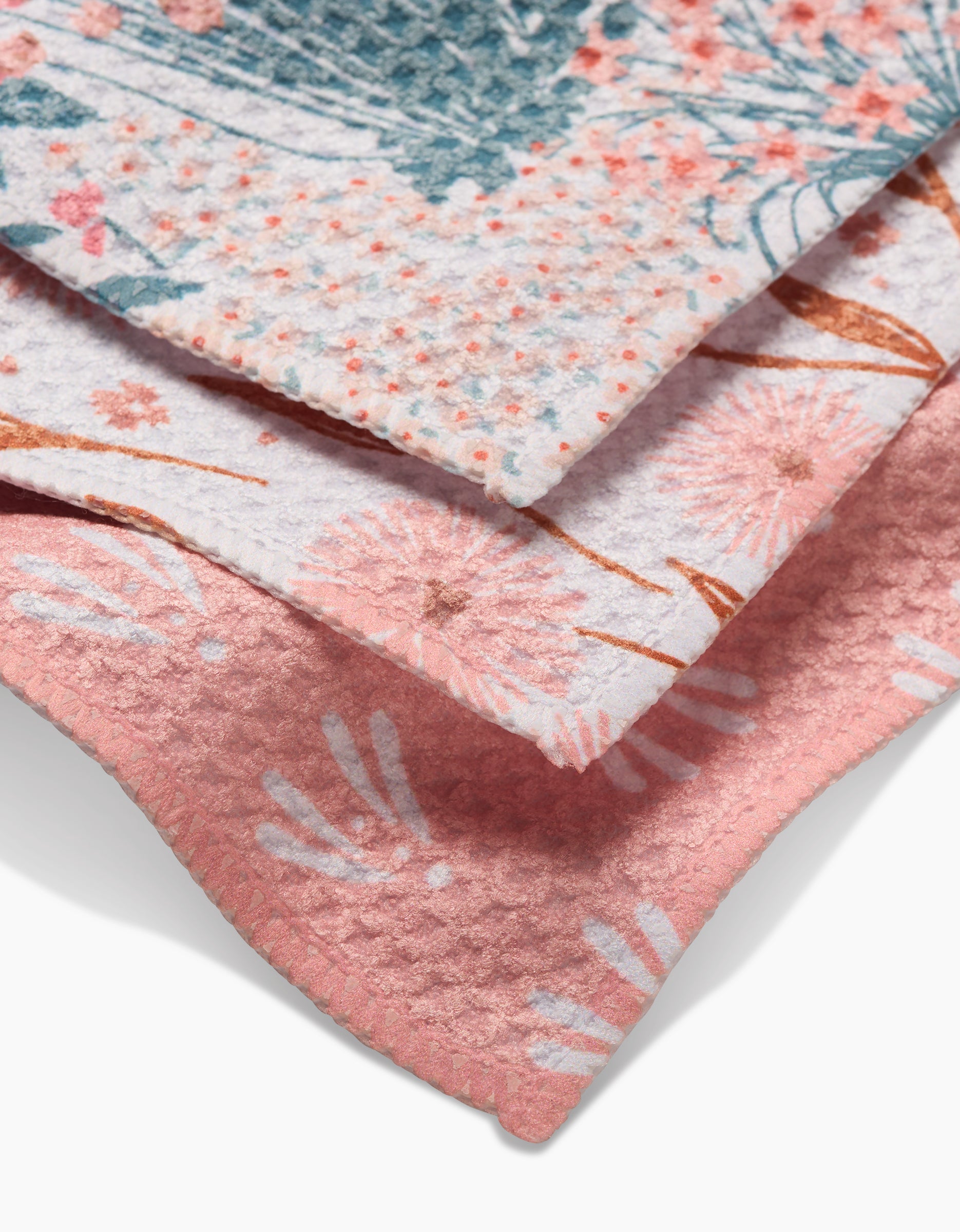 The Garden Bloom dishcloths by Hufton Studio feature three stacked cloths with pink, white, and green floral patterns. Each has a unique flower design, soft texture, and is made from recycled materials.