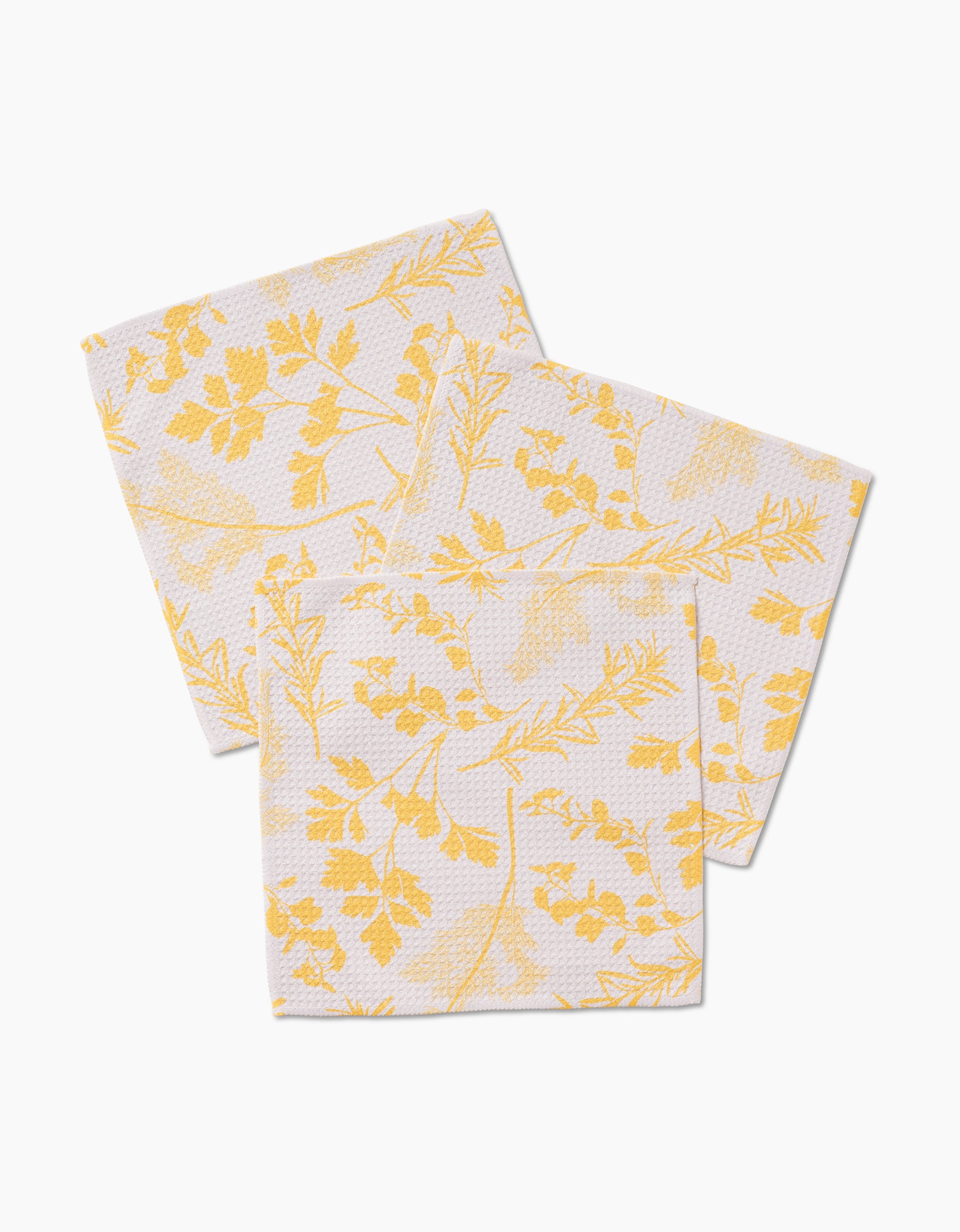 Three GEOMETRY “Garden of Gold” Geoweave fabric napkins, featuring a yellow botanical leaf and branch pattern, are arranged overlapping on a plain white background.