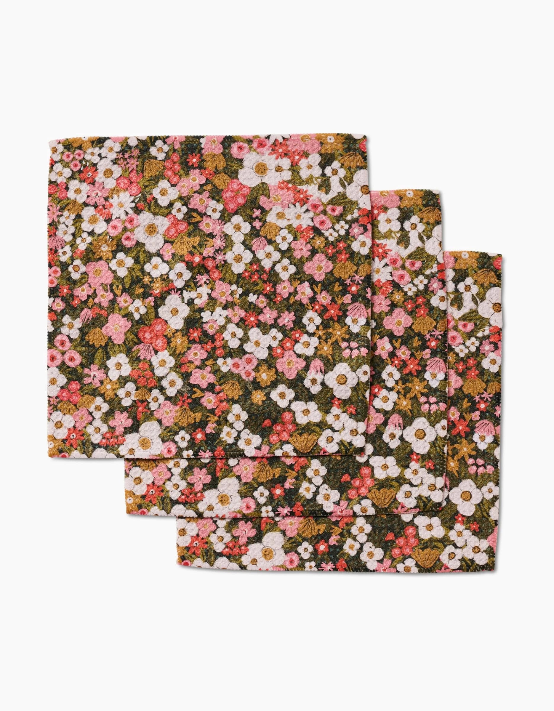 Three folded Gilded Garden napkins by Lisa Nelson, crafted from Geoweave fabric and featuring a dense floral pattern with pink, white, and orange flowers plus green and brown foliage.