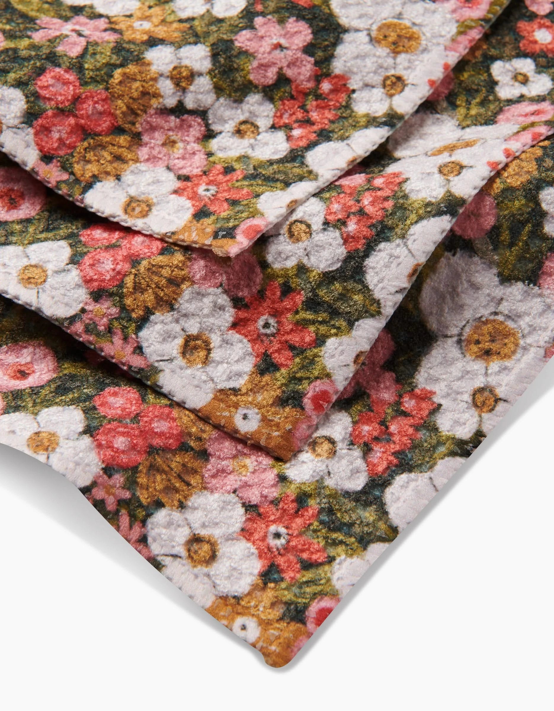 Close-up of folded Lisa Nelson Gilded Garden Geoweave dishcloth, showcasing a colorful floral pattern with white, red, pink, and yellow flowers and green leaves.