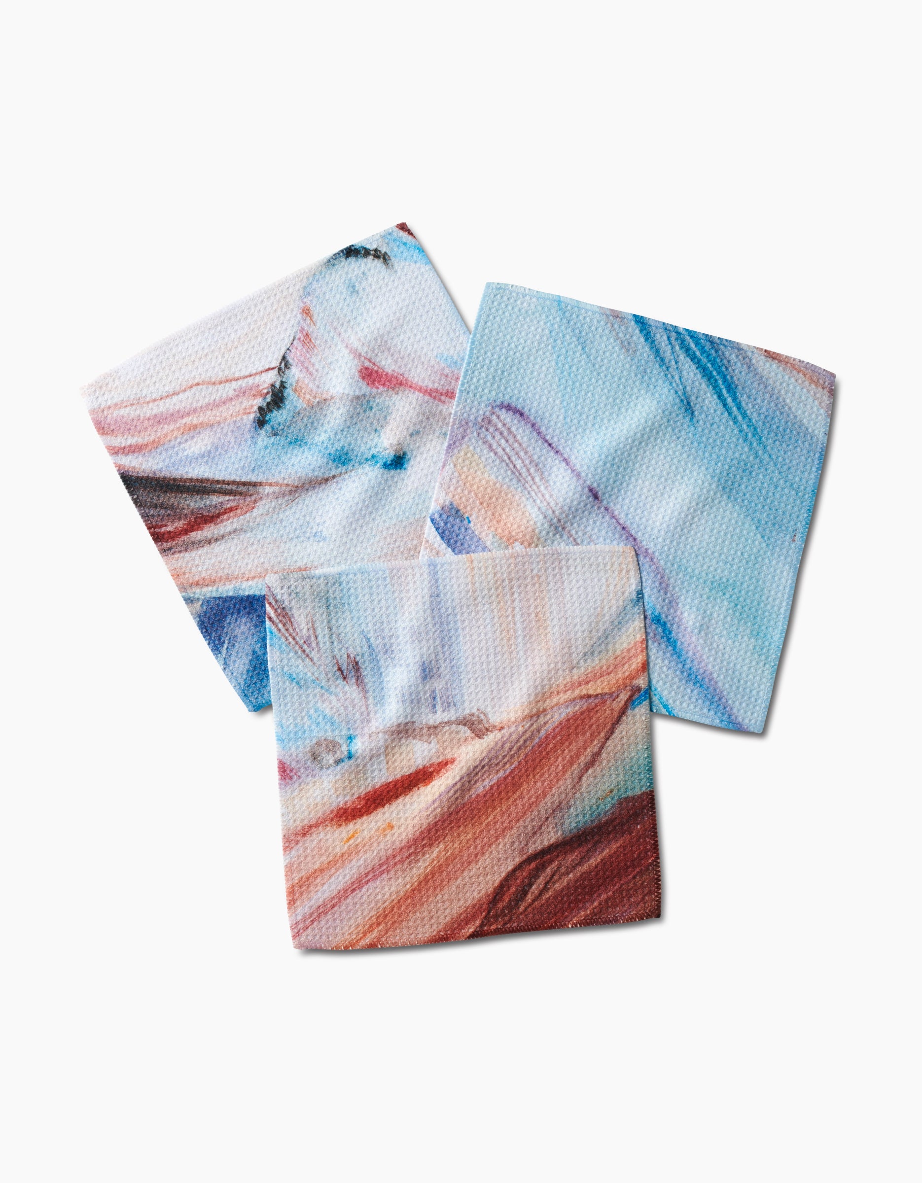 Three “Golden Hour in the Rockies” dishcloths by Kelly Peters, featuring abstract designs in blue, pink, brown, and white, overlap on a white background. Crafted from durable Geoweave fabric for excellent absorbency and quick drying.