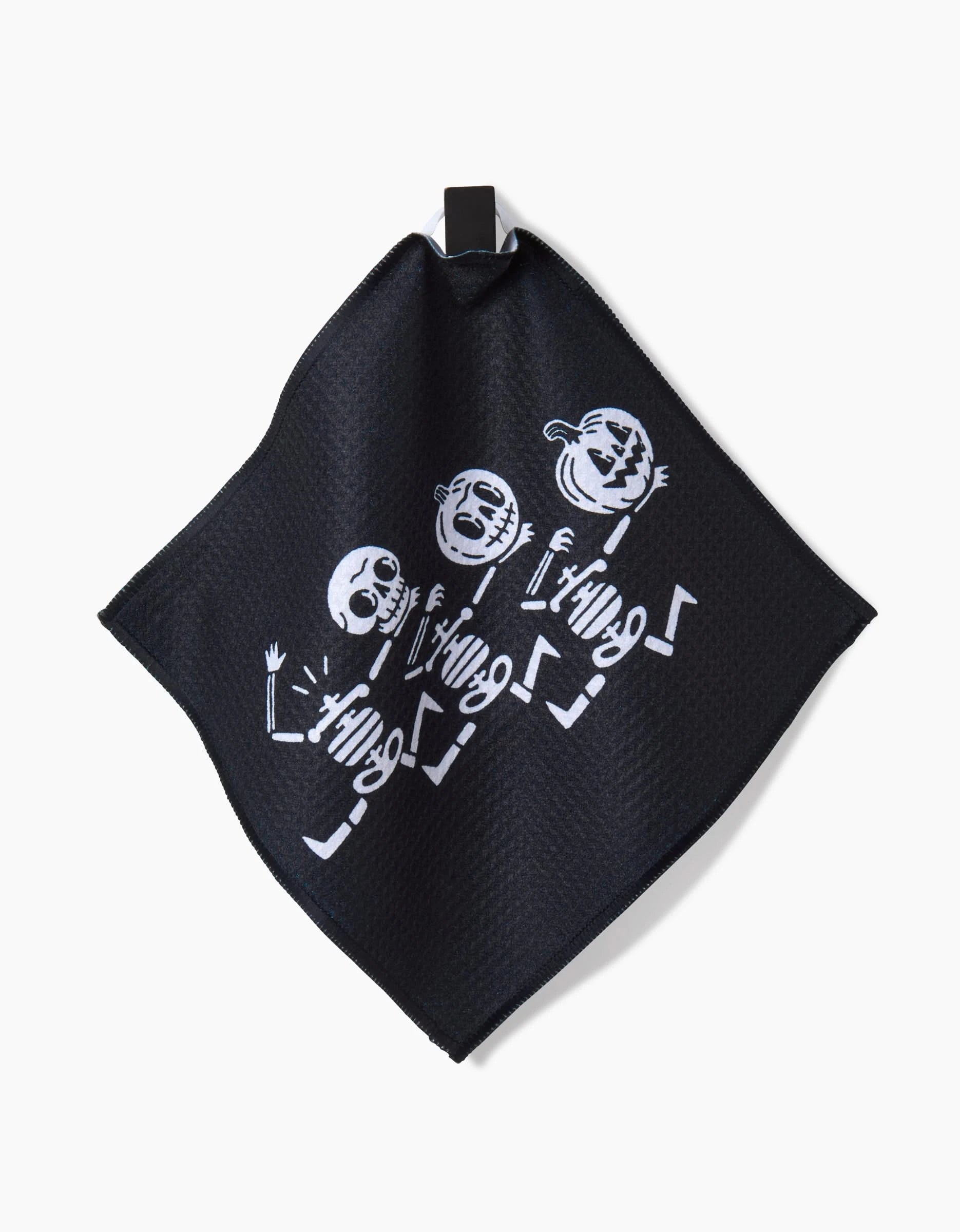 The Graveyard Smash by Carly Berry is a black cloth made from recycled materials, featuring three dancing white cartoon skeletons in unique poses and expressions, plus a small black loop in one corner for easy hanging.