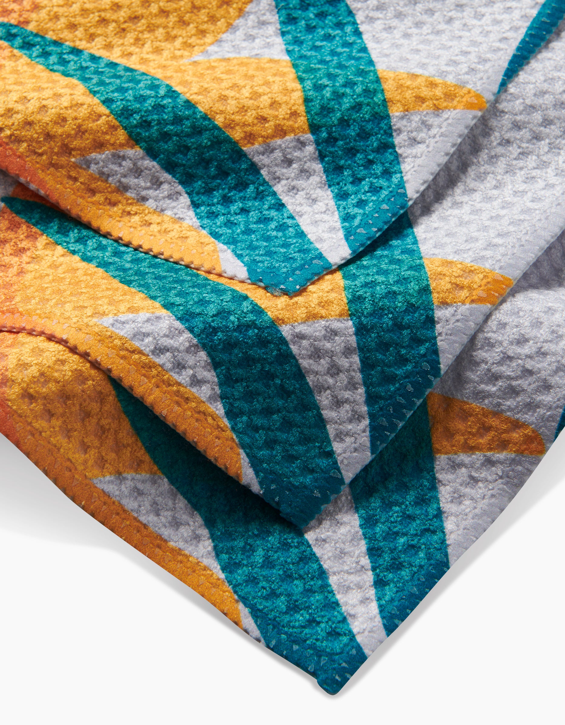 A close-up of the GEOMETRY Growth dishcloth shows its textured Geoweave fabric and colorful geometric design in teal, yellow, orange, and white with overlapping, folded layers.