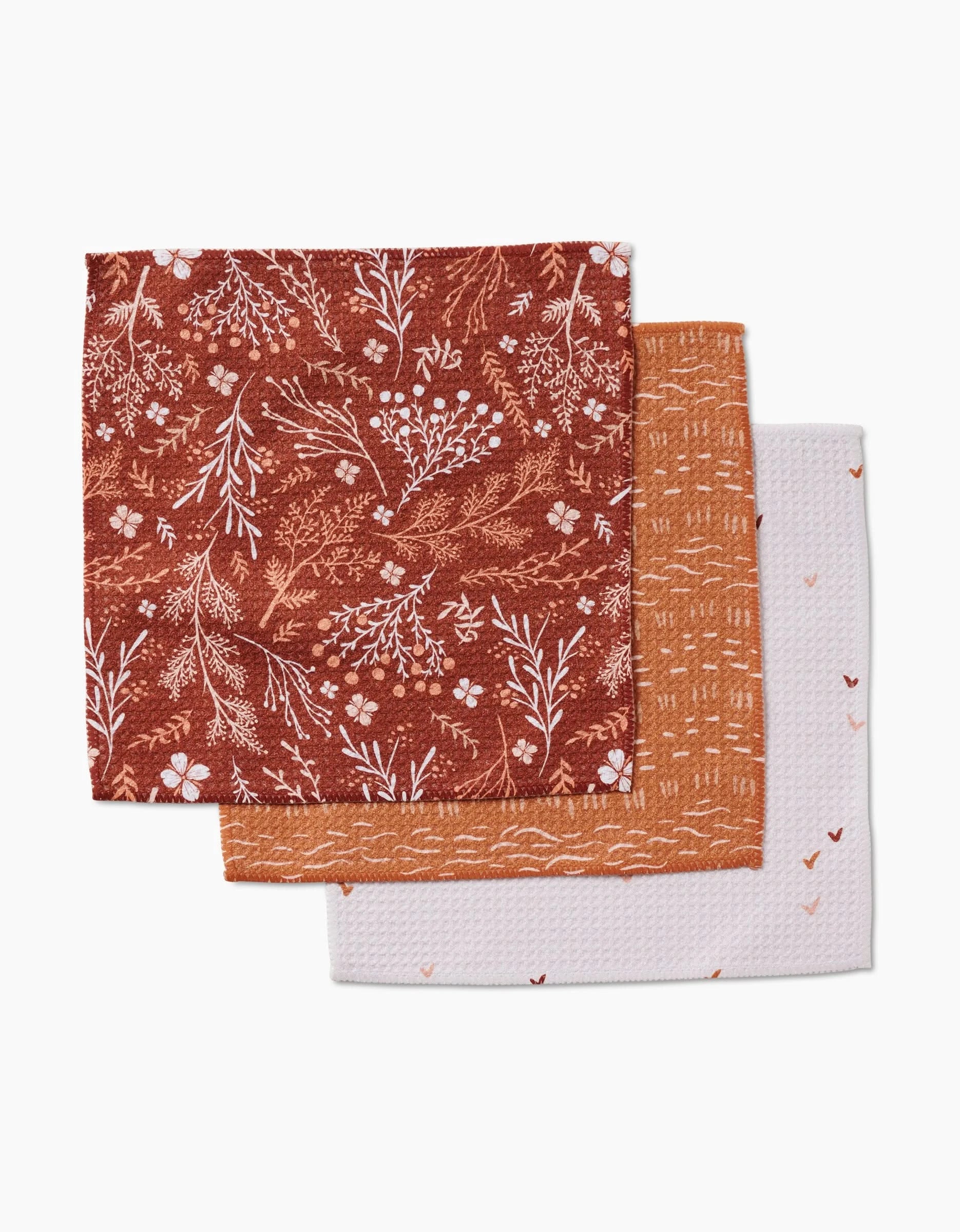 Gust of Wind by Danelys Sidron: a set of three folded recycled cloth napkins—red floral, orange geometric, and white with scattered hearts.