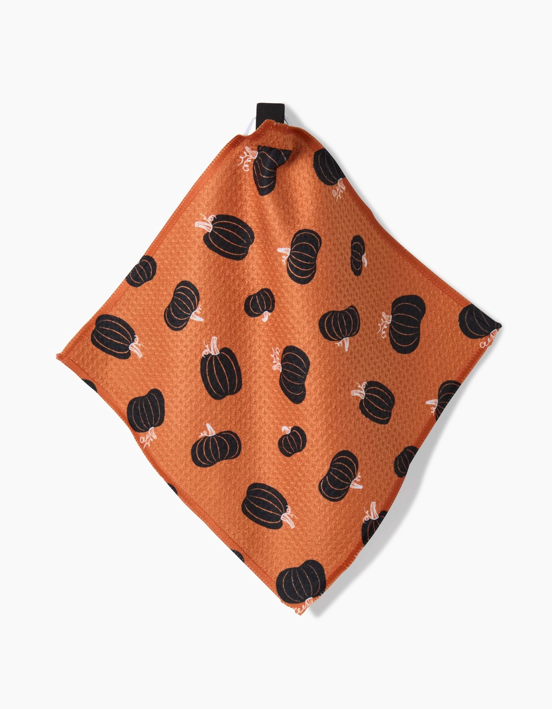 The Hufton Studio Halloween Black Pumpkins kitchen towel features a black pumpkin pattern on orange, crafted from recycled materials with a small hanging loop. Displayed against a white background.